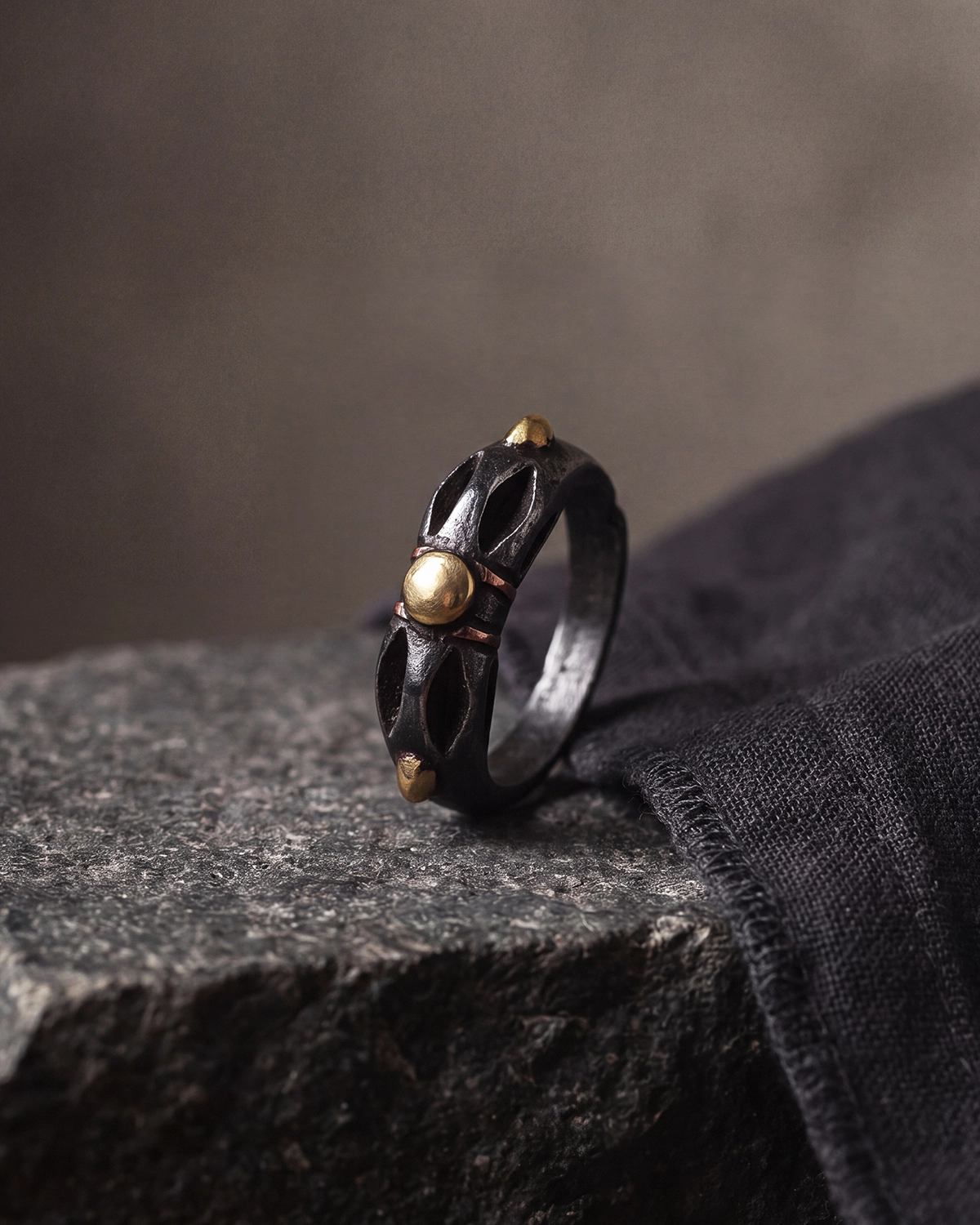 Cold Iron Vajra Dorje ring standing on a dark stone surface with a soft gray background.
