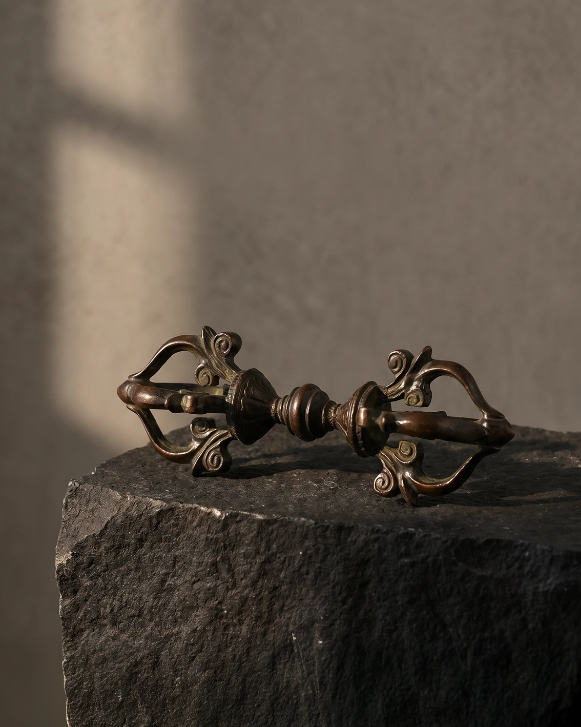 Copper-plated Vajra altar decor resting on a dark stone plinth against a warm gray wall with soft side light.