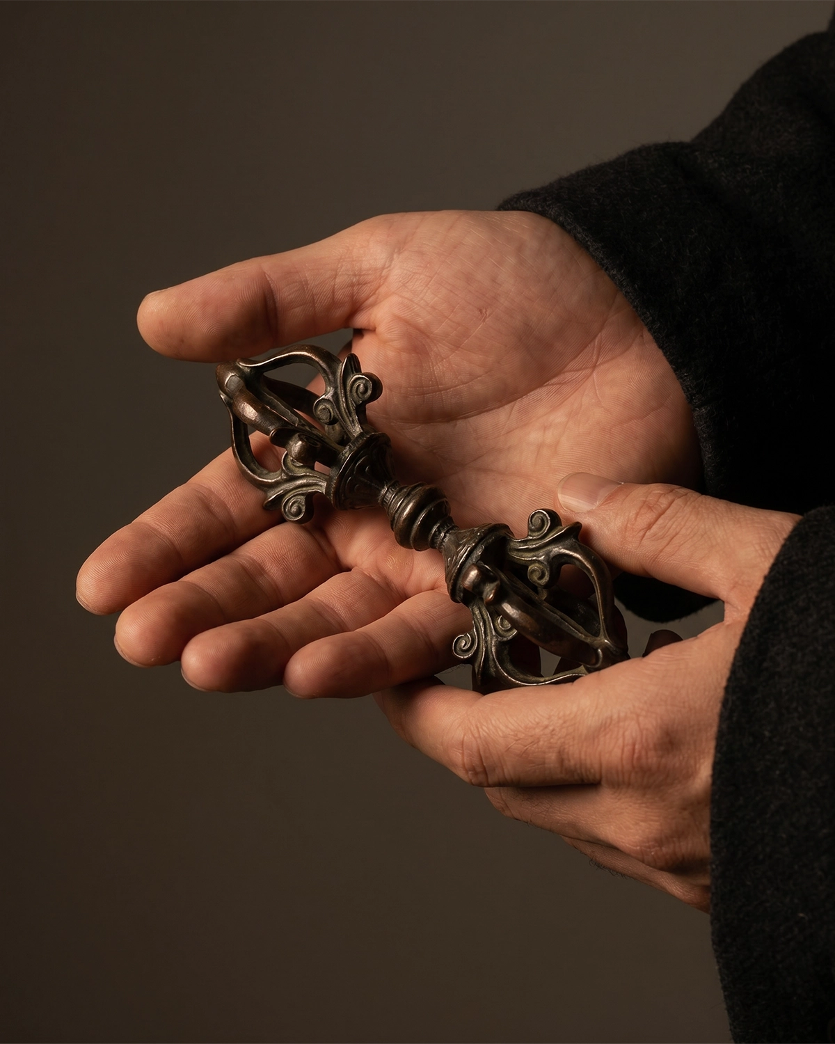 Copper-plated Vajra altar object held in adult hands to show its compact hand-sized scale.