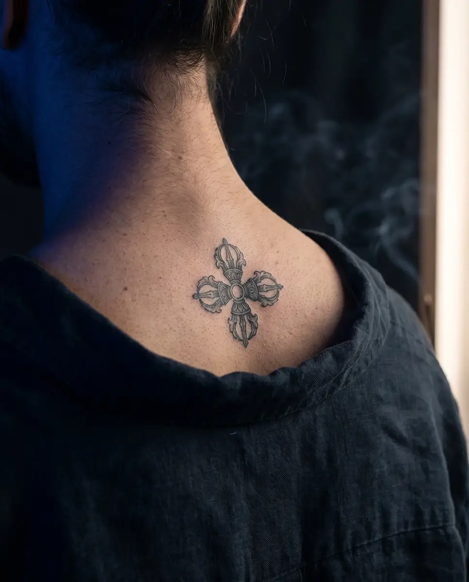 A double dorje tattoo etched gracefully on the upper back of a person wearing dark linen, symbolizing indestructible tattoos for wisdom and inner grounding.