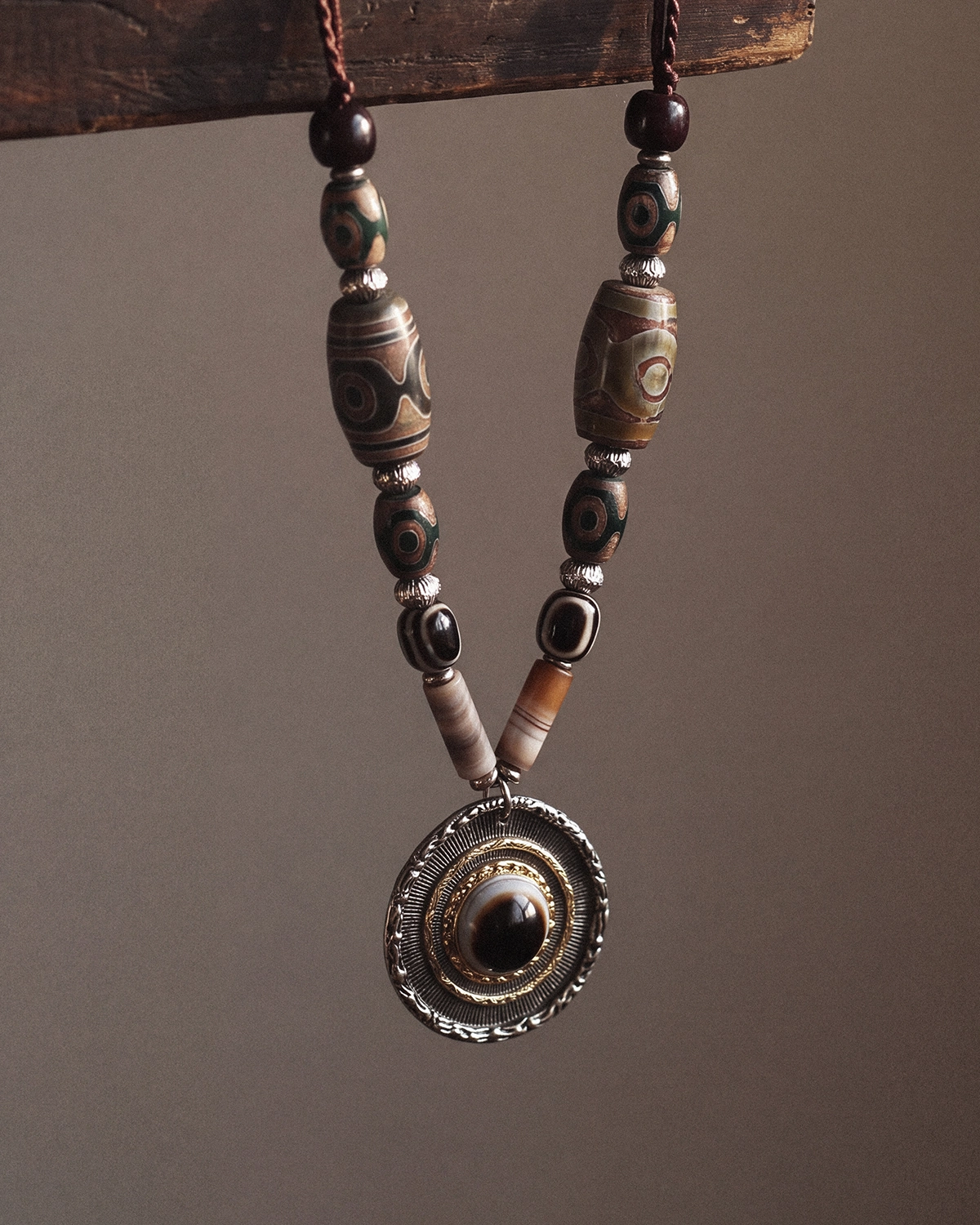 Close-up of a hanging dzi bead necklace showing patterned agate beads, metal spacers, and the round eye pendant.