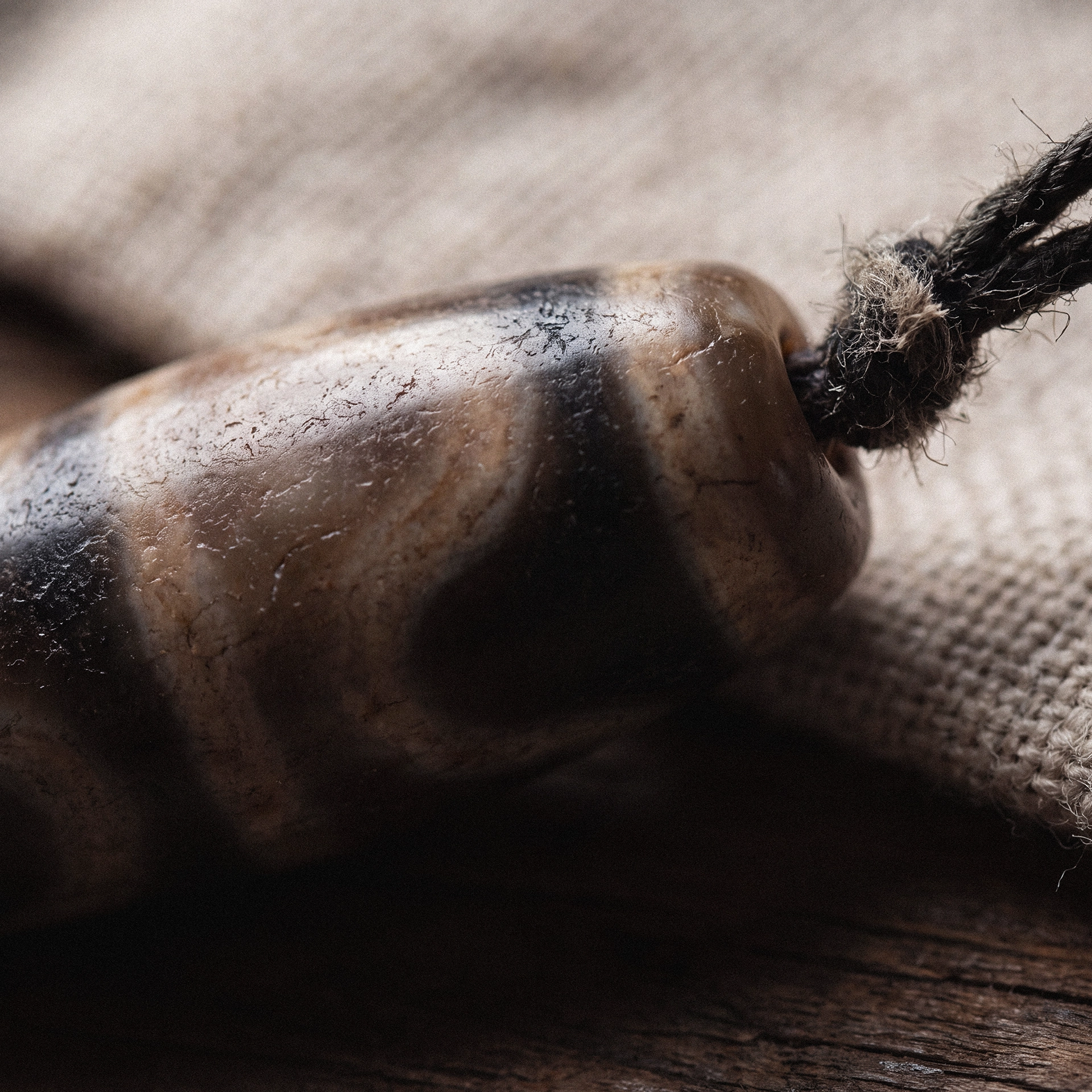 Extreme close-up of a patterned dzi bead's banded surface and worn dark cord threaded through its hole.