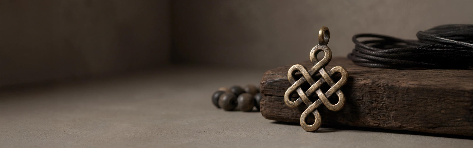 Endless Knot inspired aged bronze pendant arranged on weathered wood with muted beads, dark cord, and quiet wabi-sabi atmosphere.