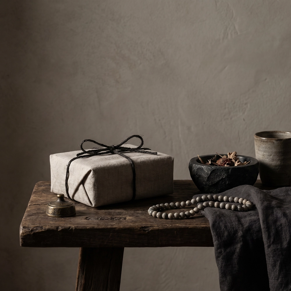 {"default":"Square mobile banner showing a linen-wrapped gift with dark cord, muted beads, ceramic cup, black stone bowl, dried flowers, and quiet ritual gifting atmosphere."}

