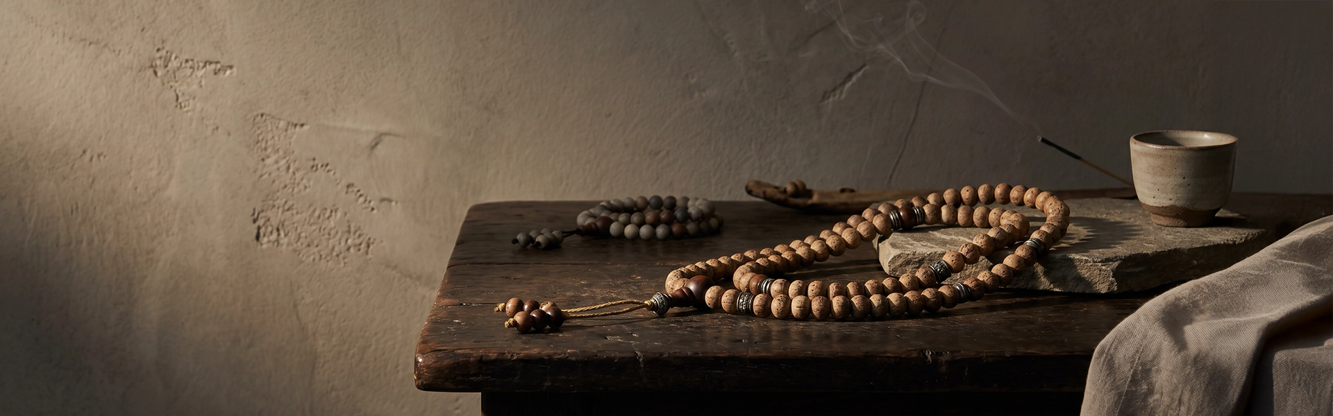 Bodhi seed mala and prayer beads on dark wood and raw stone in a quiet Western wabi-sabi ritual setting with soft incense smoke.
