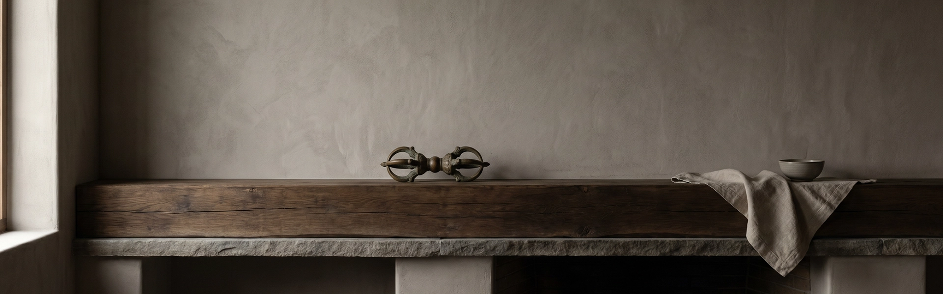 Mantel and ledge scene with a Vajra-inspired symbolic object on an aged wooden fireplace mantel, linen cloth, ceramic bowl, and quiet wabi-sabi home atmosphere.