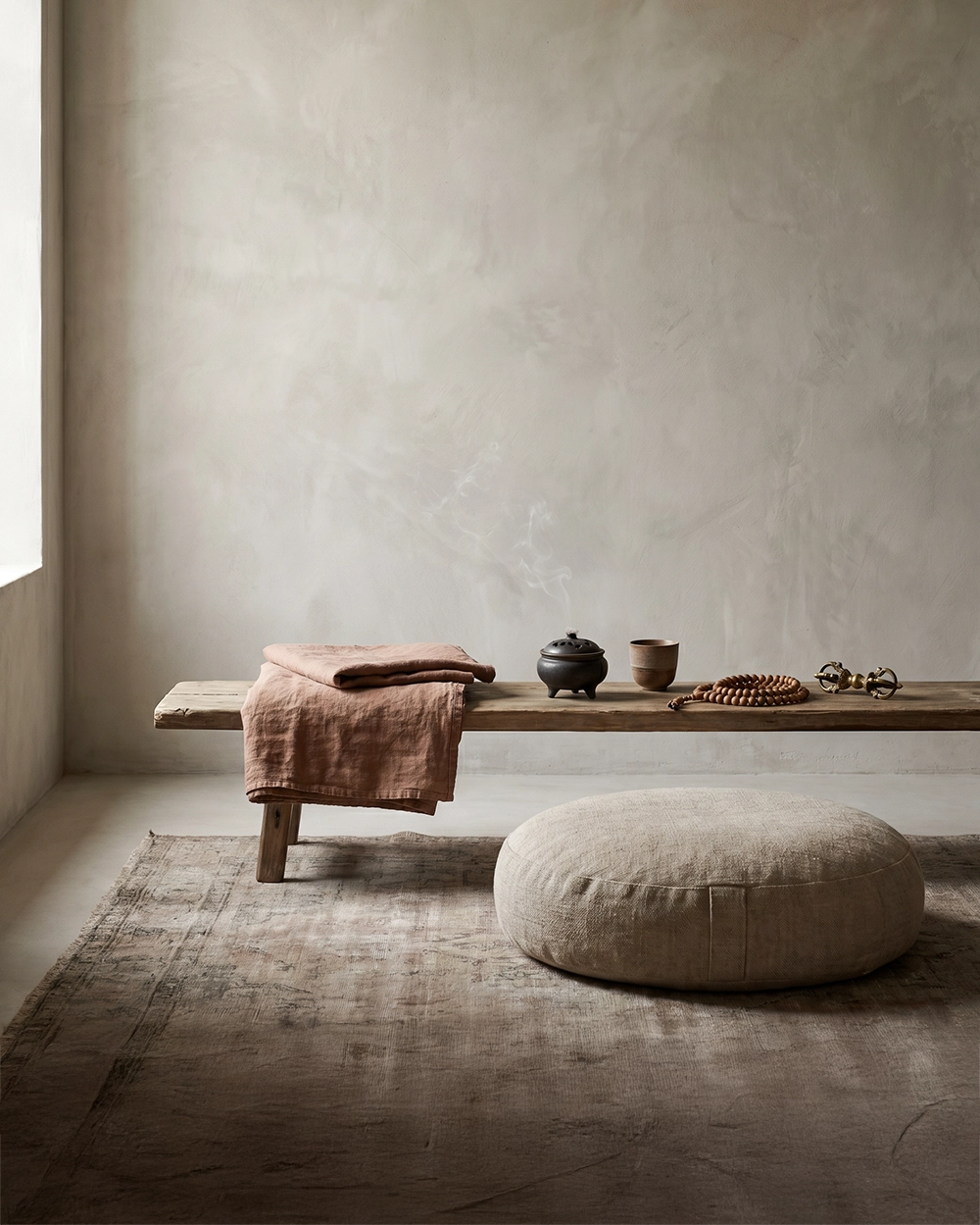 A serene meditation corner with mala beads, a Vajra object, incense, ceramic cup, folded linen, and a floor cushion in a quiet wabi-sabi room