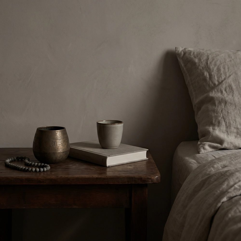 {"default":"Square mobile banner showing a quiet bedside table with muted beads, ceramic vessel, cup, closed book, linen pillow, and restrained wabi-sabi styling."}
