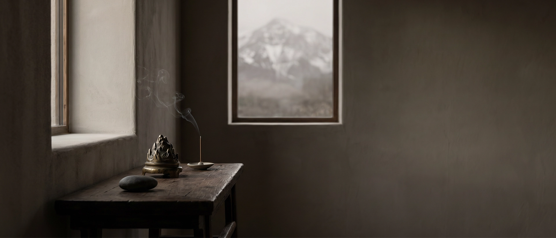 A quiet wooden table with incense, stone, and a small ritual object beside a window overlooking a distant mountain in a wabi-sabi interior