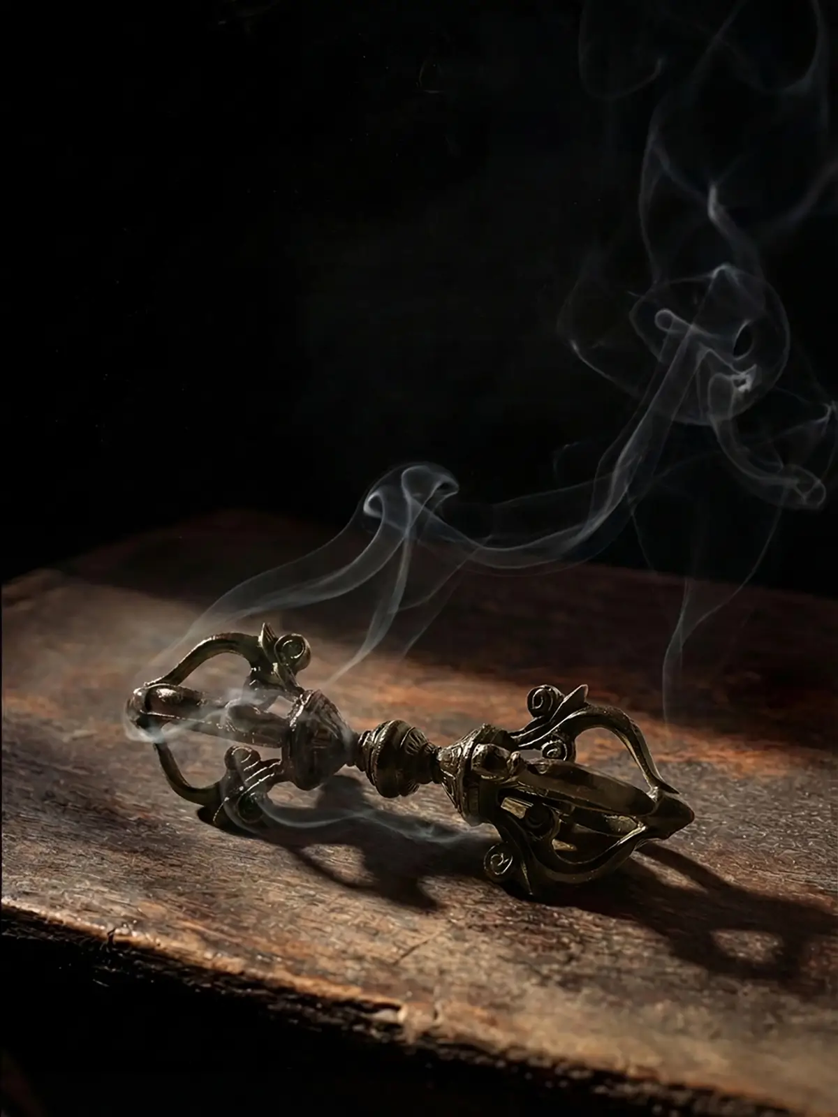 Small solid copper vajra dorje altar decor resting on a reclaimed wooden altar with drifting incense smoke for a zen meditation room