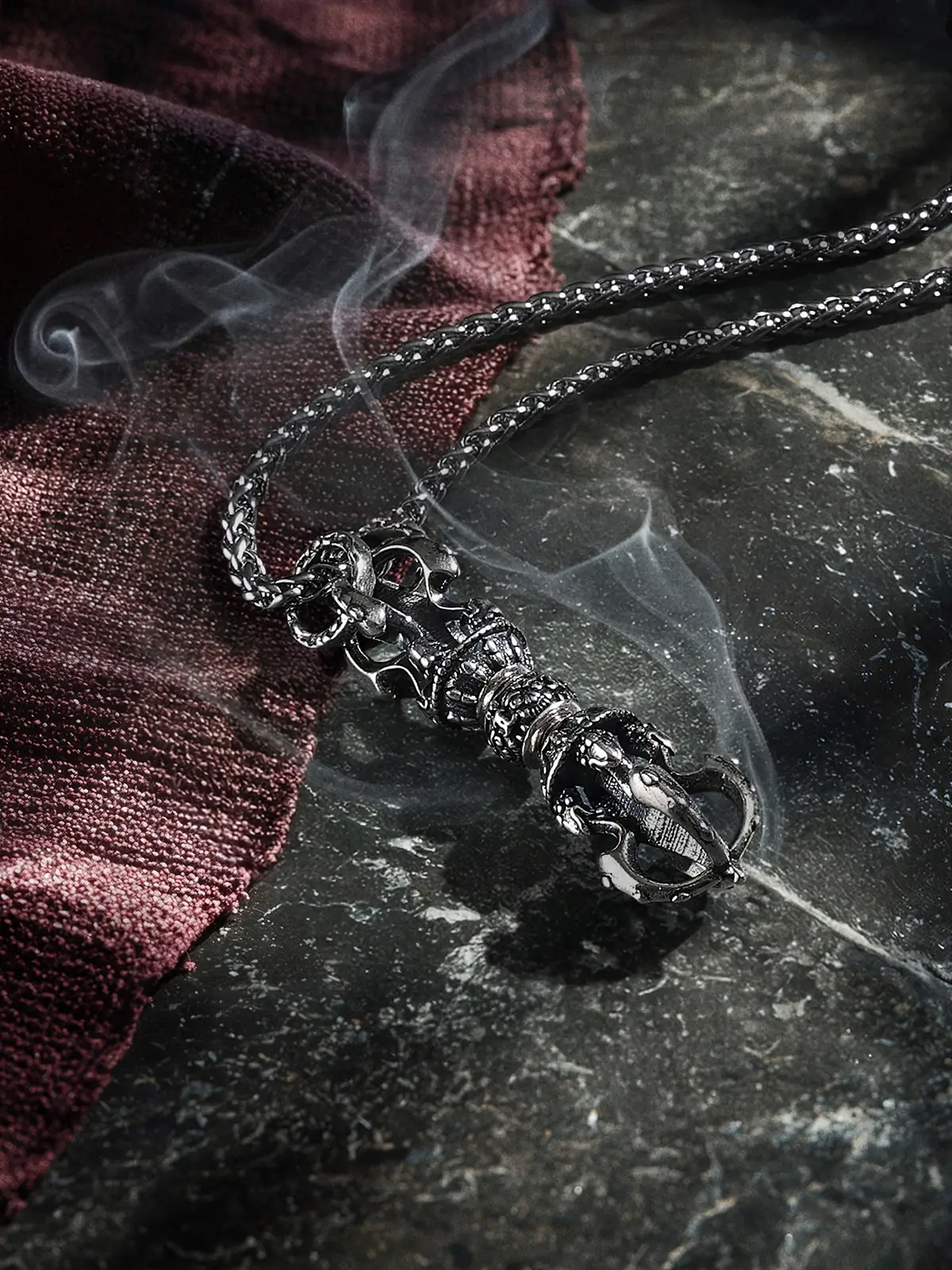 A Spinning Dorje Amulet resting on maroon monk's cloth with incense smoke. The rotatable center represents the turning of the Dharma wheel. Tibetan altar decor inspiration for sacred spaces.