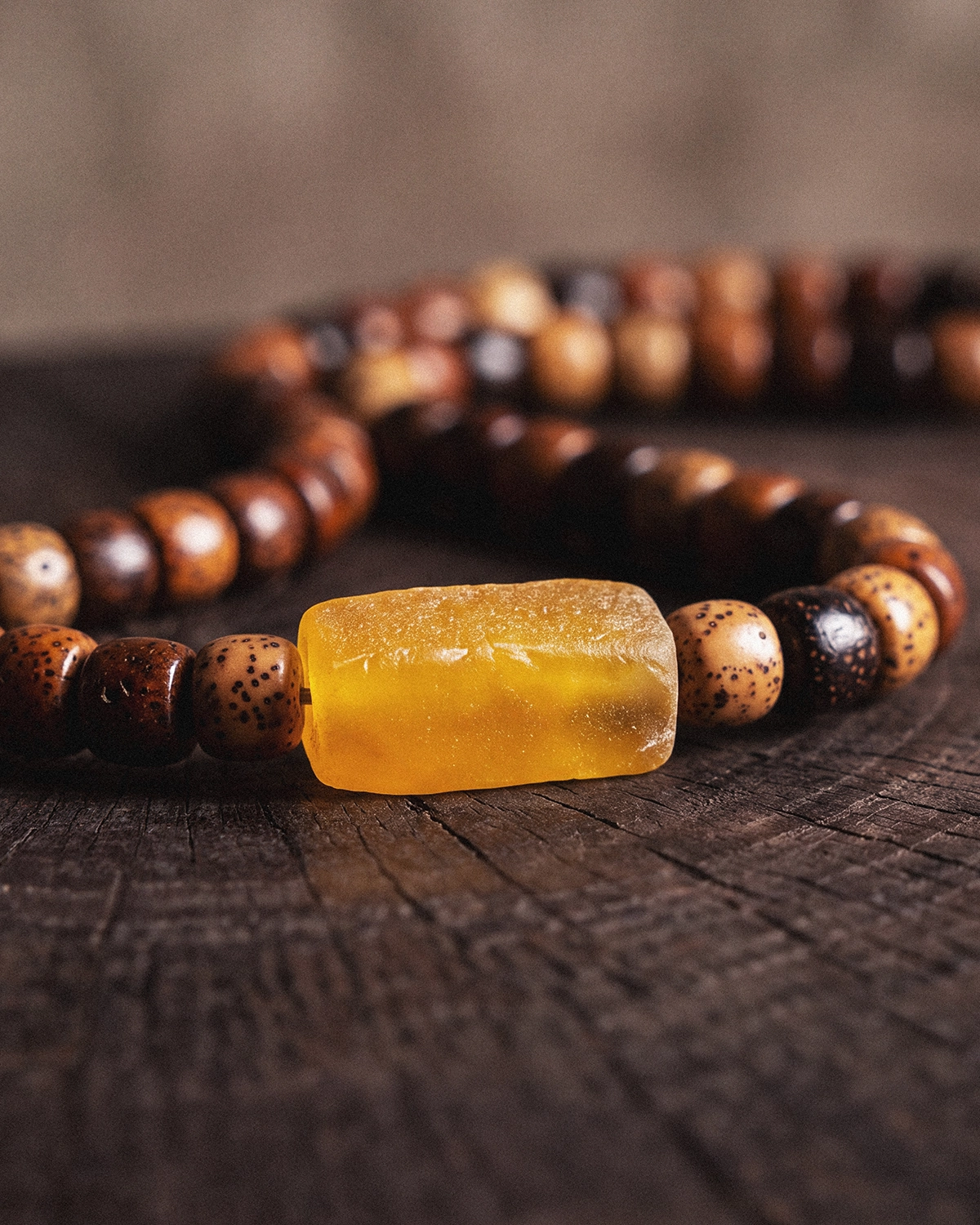 Close-up of a translucent yellow beeswax barrel bead strung between speckled star and moon bodhi seed beads on a dark wooden surface.