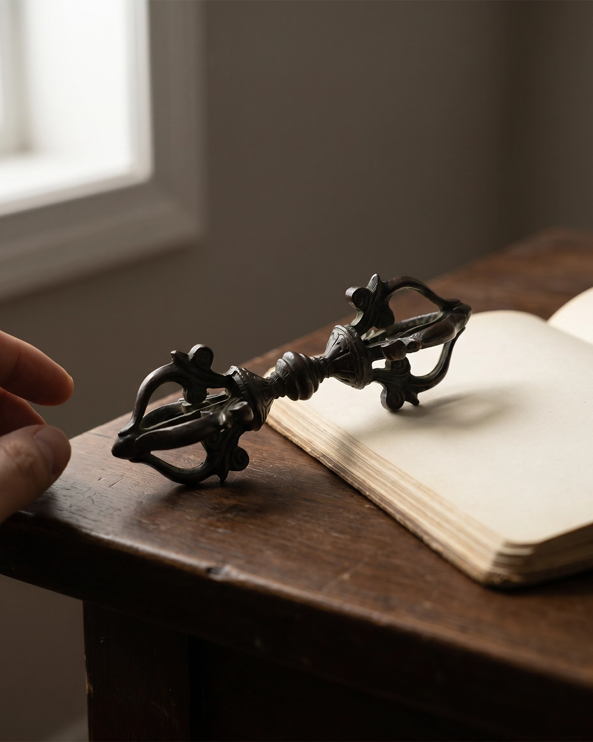 Vajra altar decor placed on a wooden desk beside an open book with a hand nearby in a quiet ritual workspace.