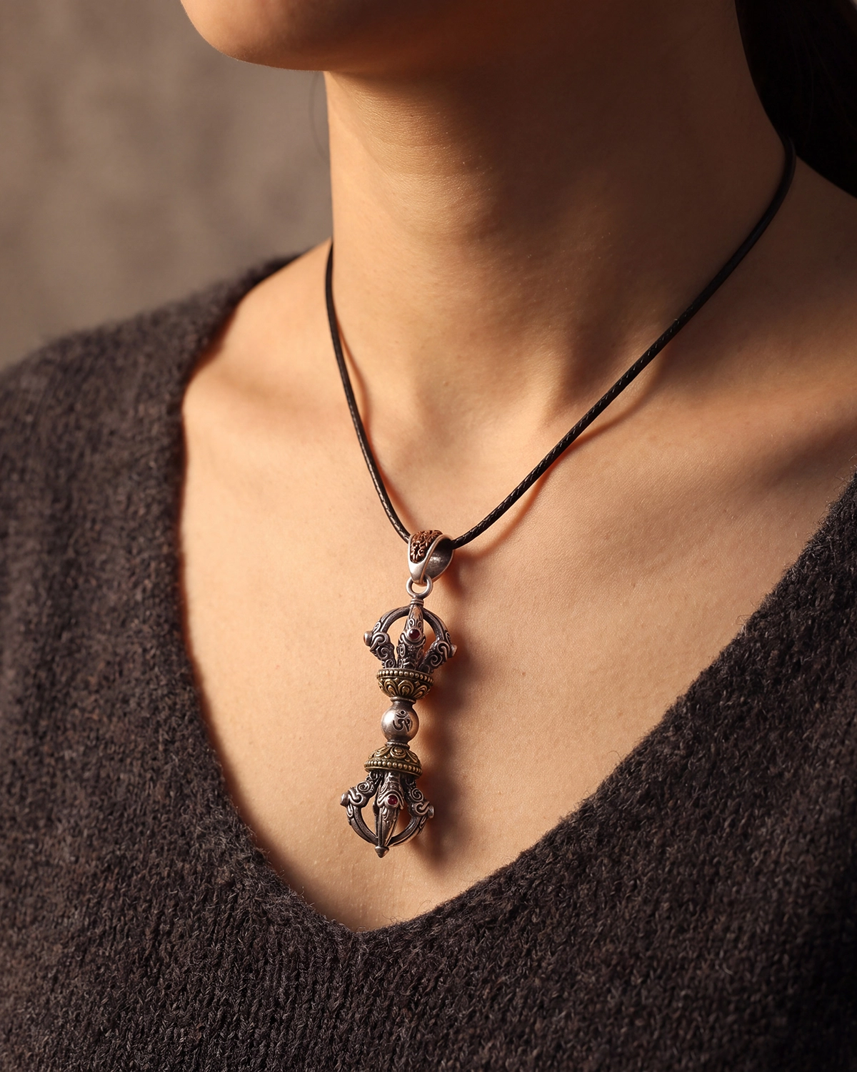 Brass Vajra Dorje pendant worn on a black cord against a neck and collarbone with a dark knit top.