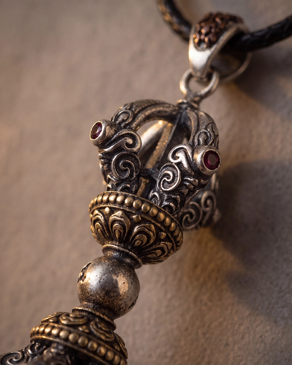 Close-up of a Vajra pendant showing carved prongs, red inlays, aged patina, and mixed-tone metal details.