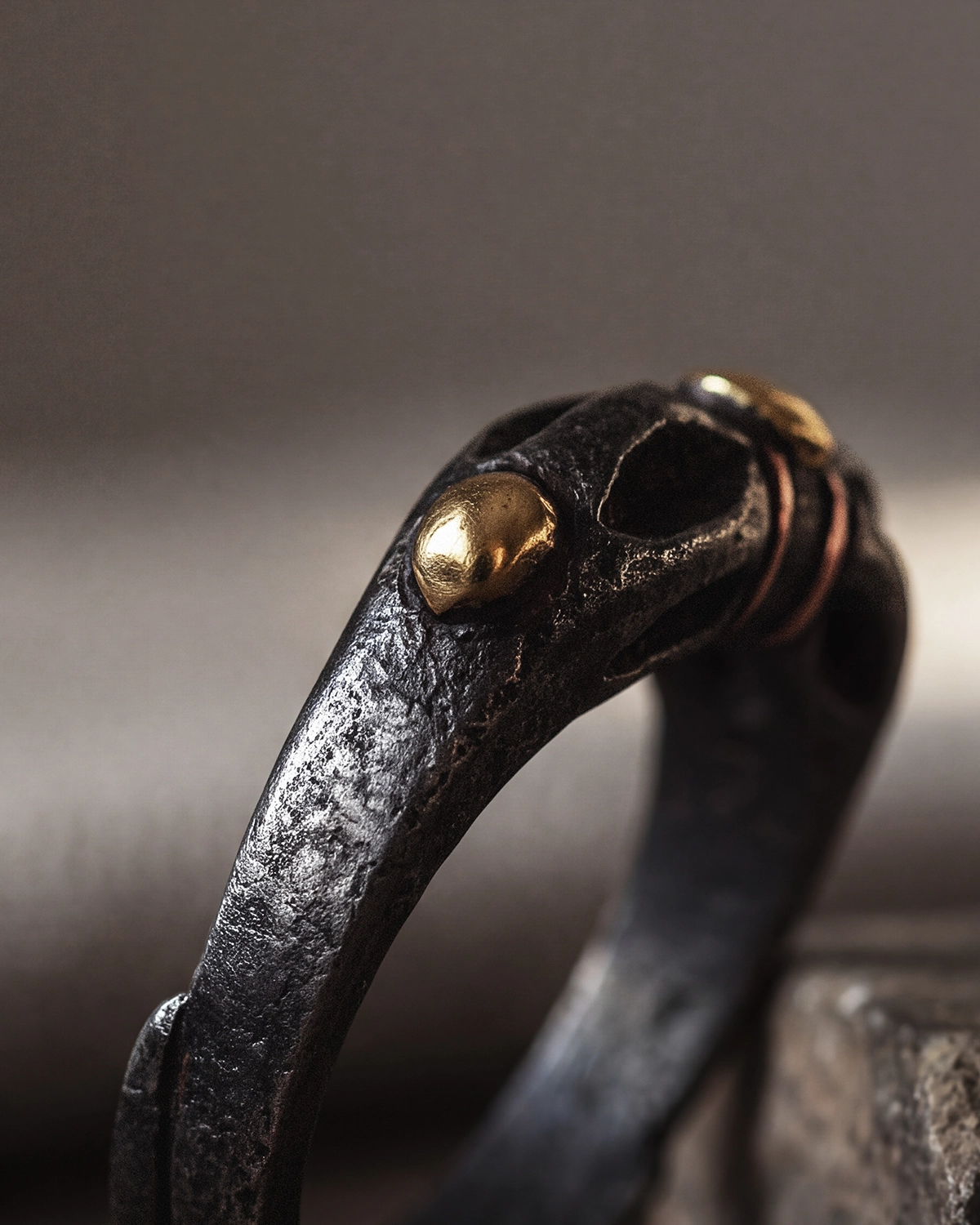 Close-up of a Tibetan-inspired vajra ring showing a polished gold-toned bead accent and copper inlay set into the side of the dark iron band.