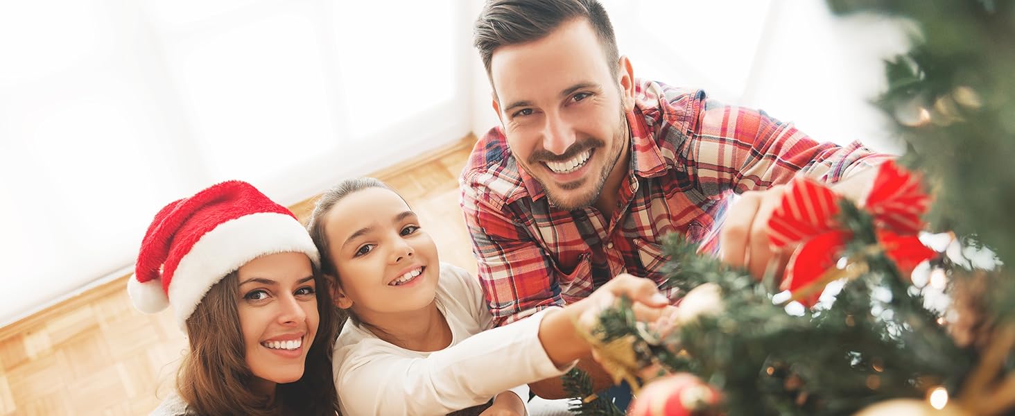 Kerstboom met ornamenten op de voorgrond. Mensen versieren een boom, één draagt een kerstmuts. Feestelijke sfeer met een glimlach en een duidelijke kerstsfeer