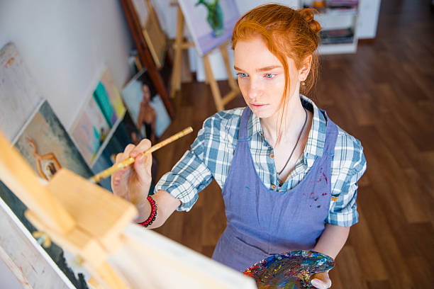 Concentrated woman painter holding art palette and painting on canvas stock photo