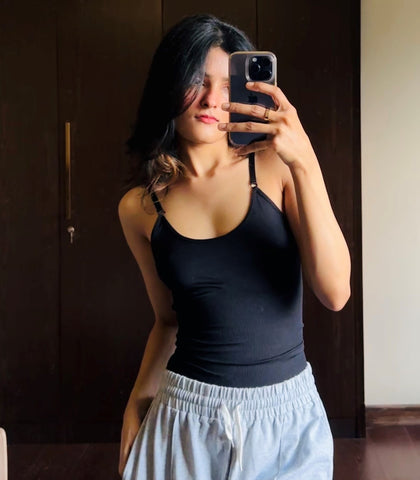 A woman taking a mirror selfie, wearing a black halter-neck top and light blue drawstring pants.