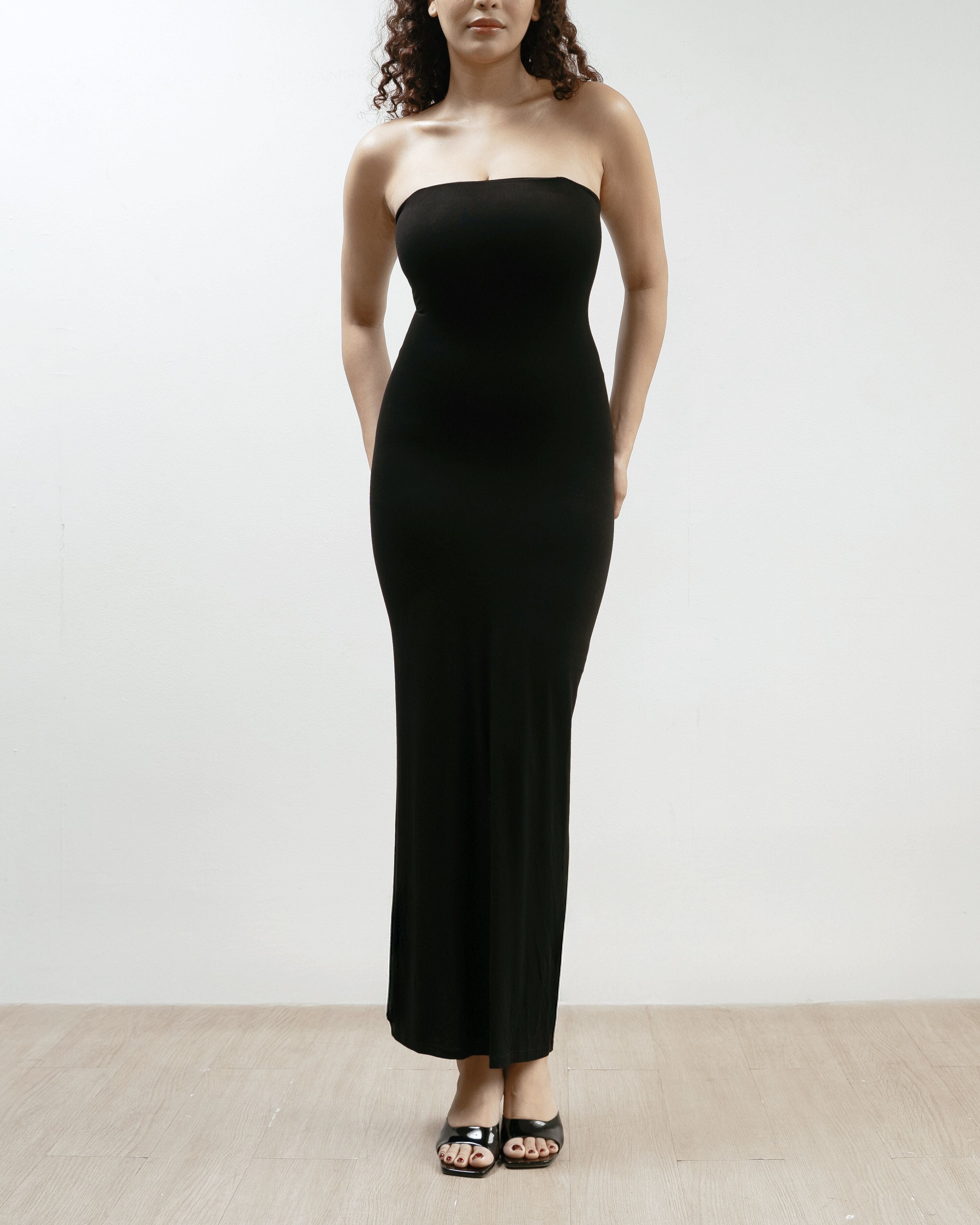 Woman wearing a black strapless dress on a plain background.