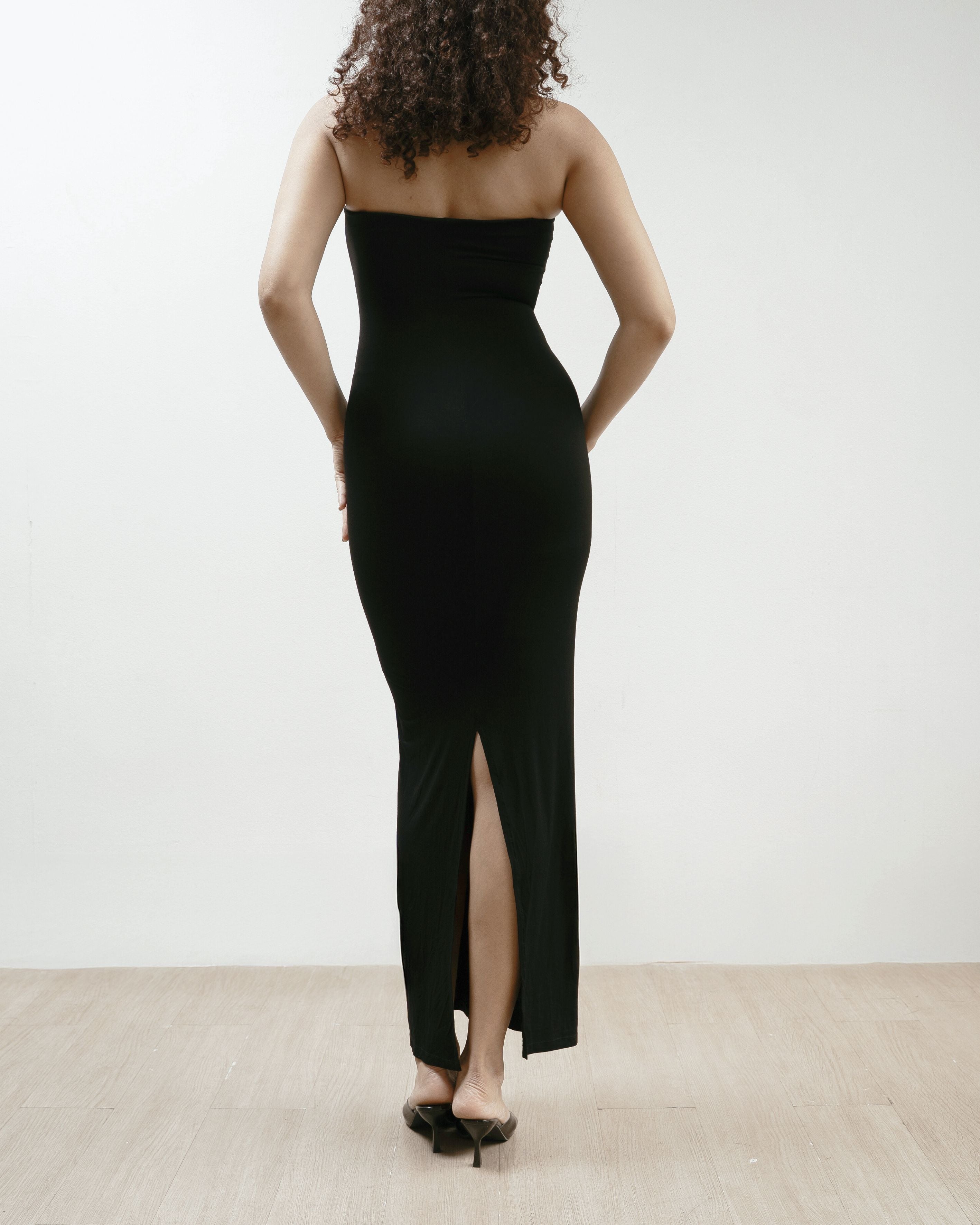 Woman wearing a black strapless dress with on a plain background.