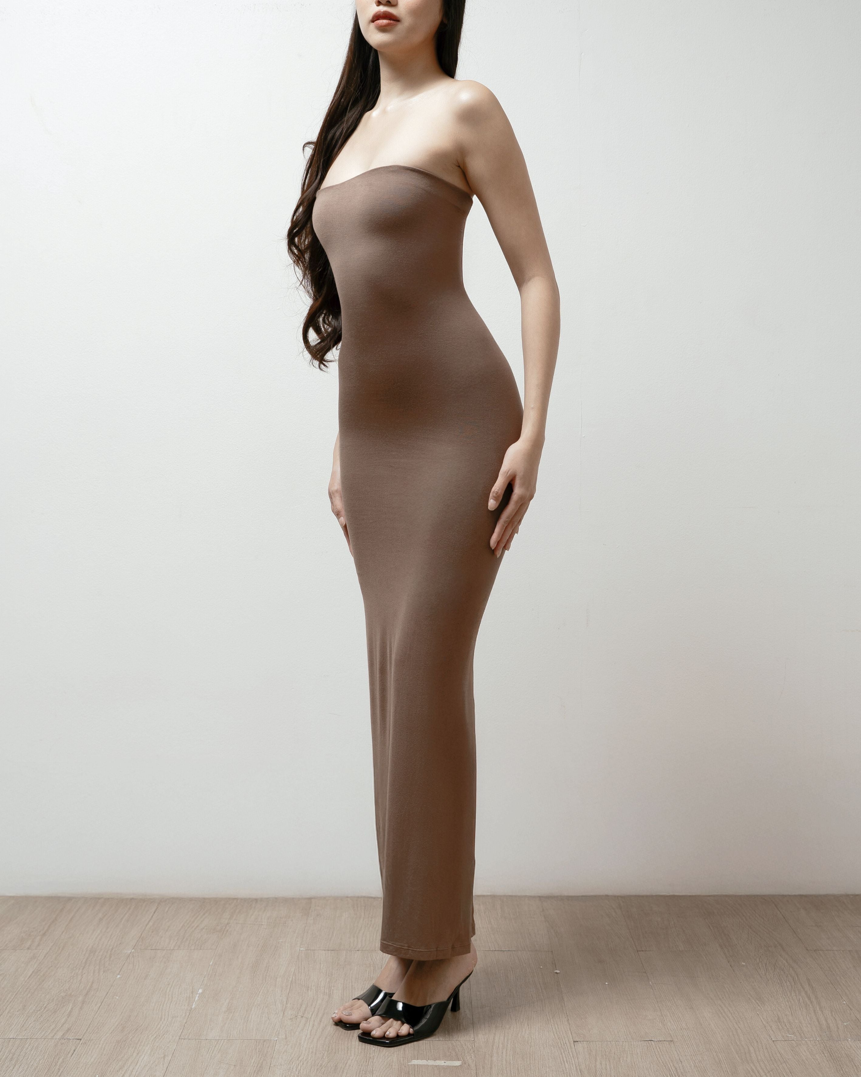 Woman wearing a brown strapless dress on a plain background.