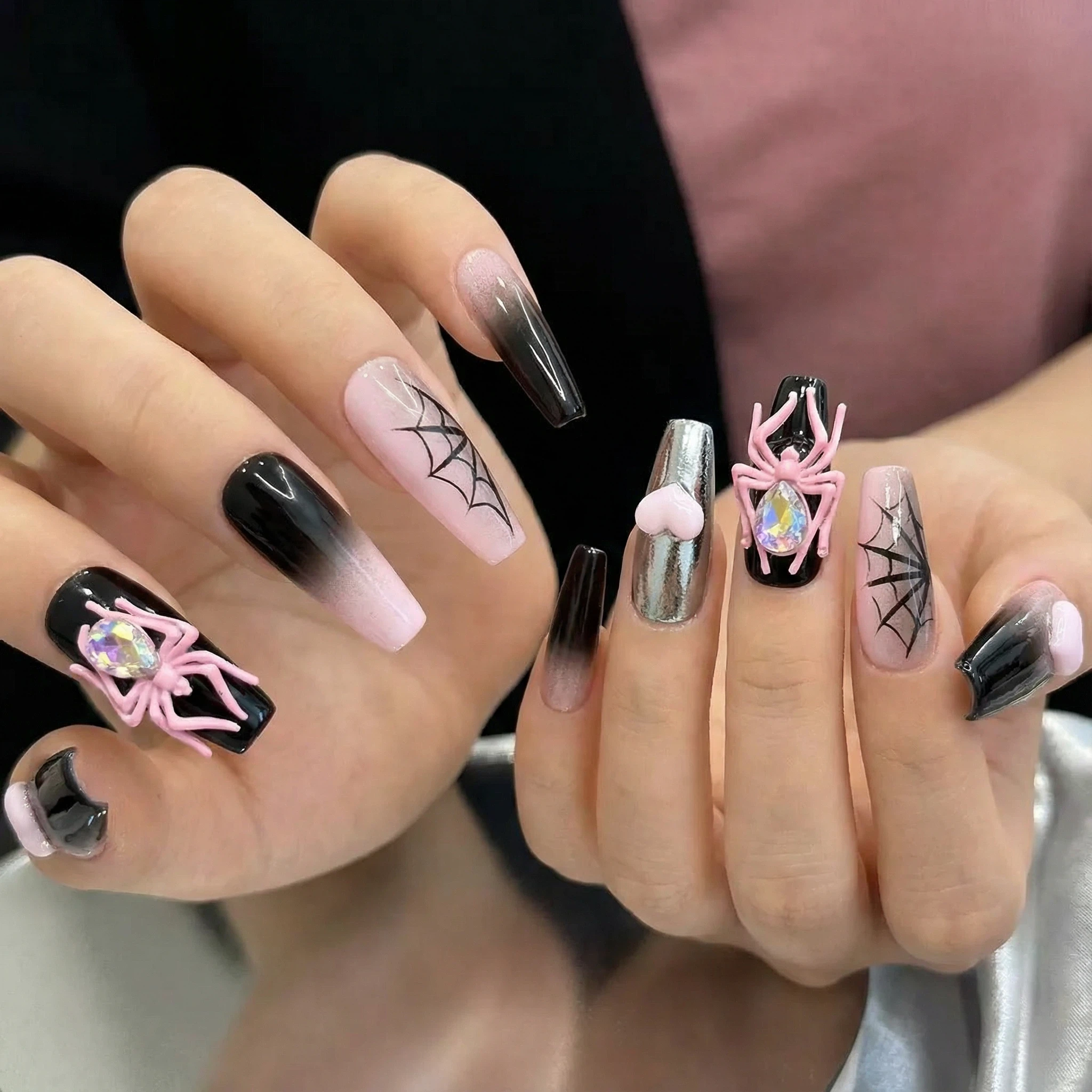 alt="Hands wearing pink and black ombre press on nails with 3D pink spider, web design and chrome heart accents"