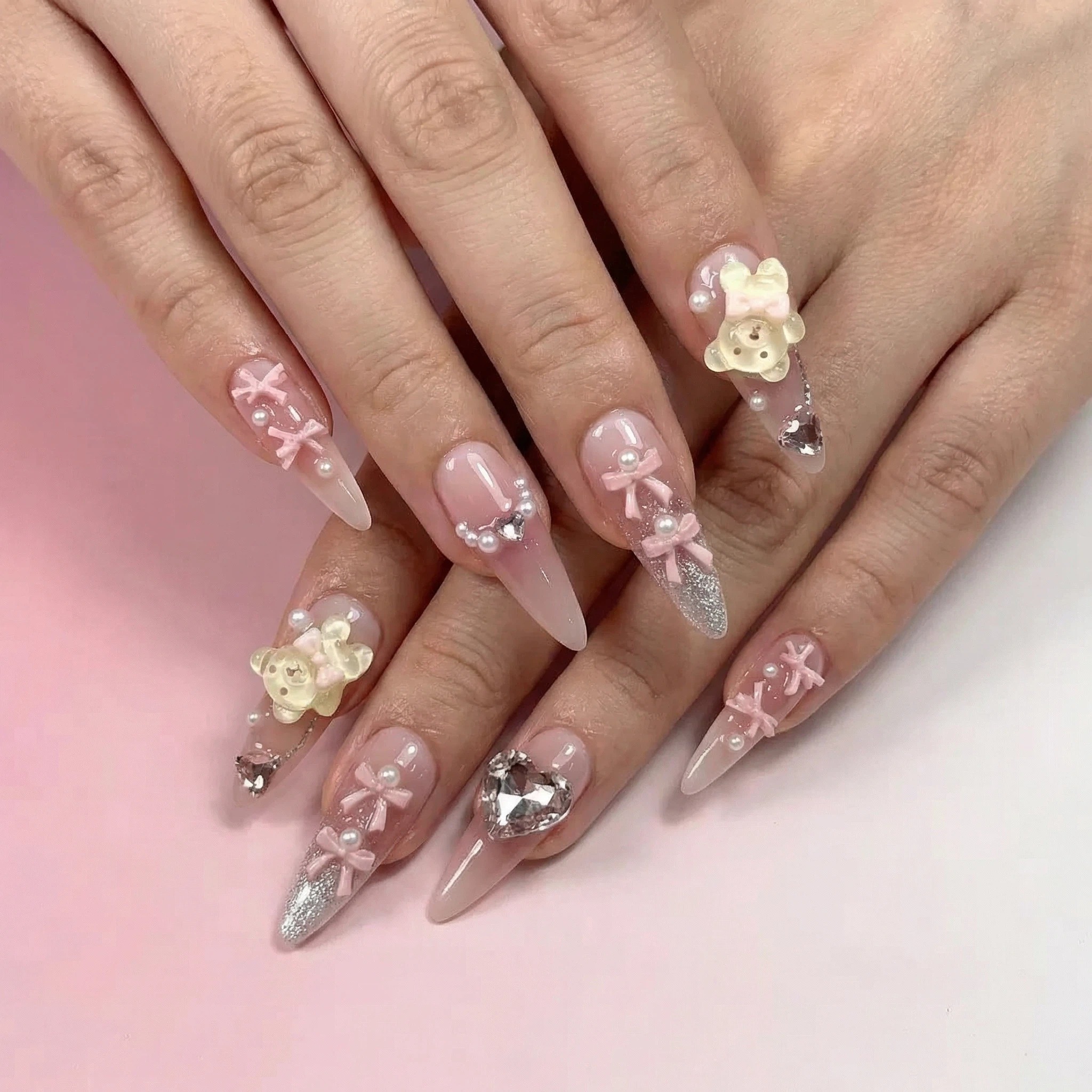 Long stiletto blush pink press on nails with 3D flowers, bows, and crystal embellishments on hands