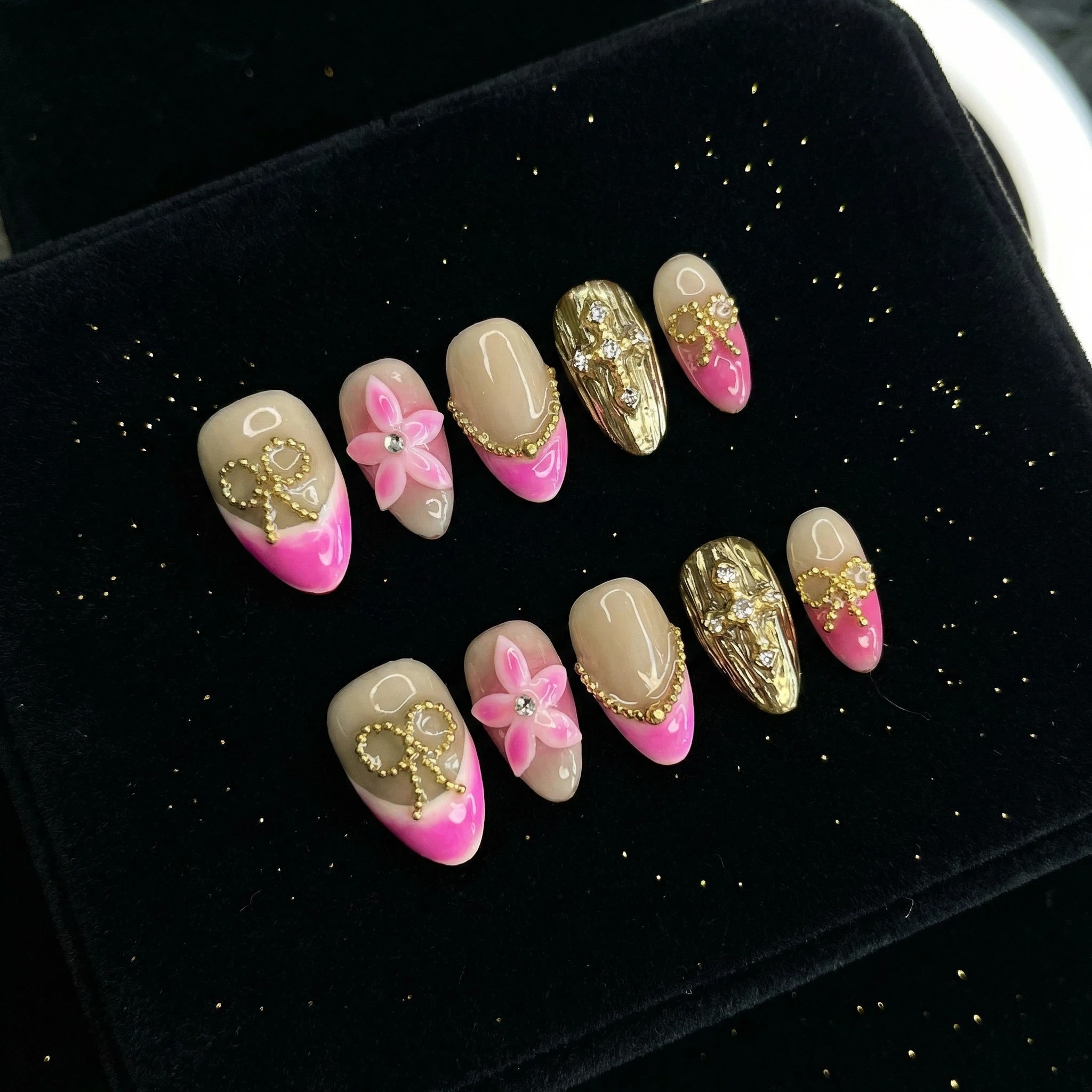 Press-on nails laid out on black background with hot pink French tips and gold glitter