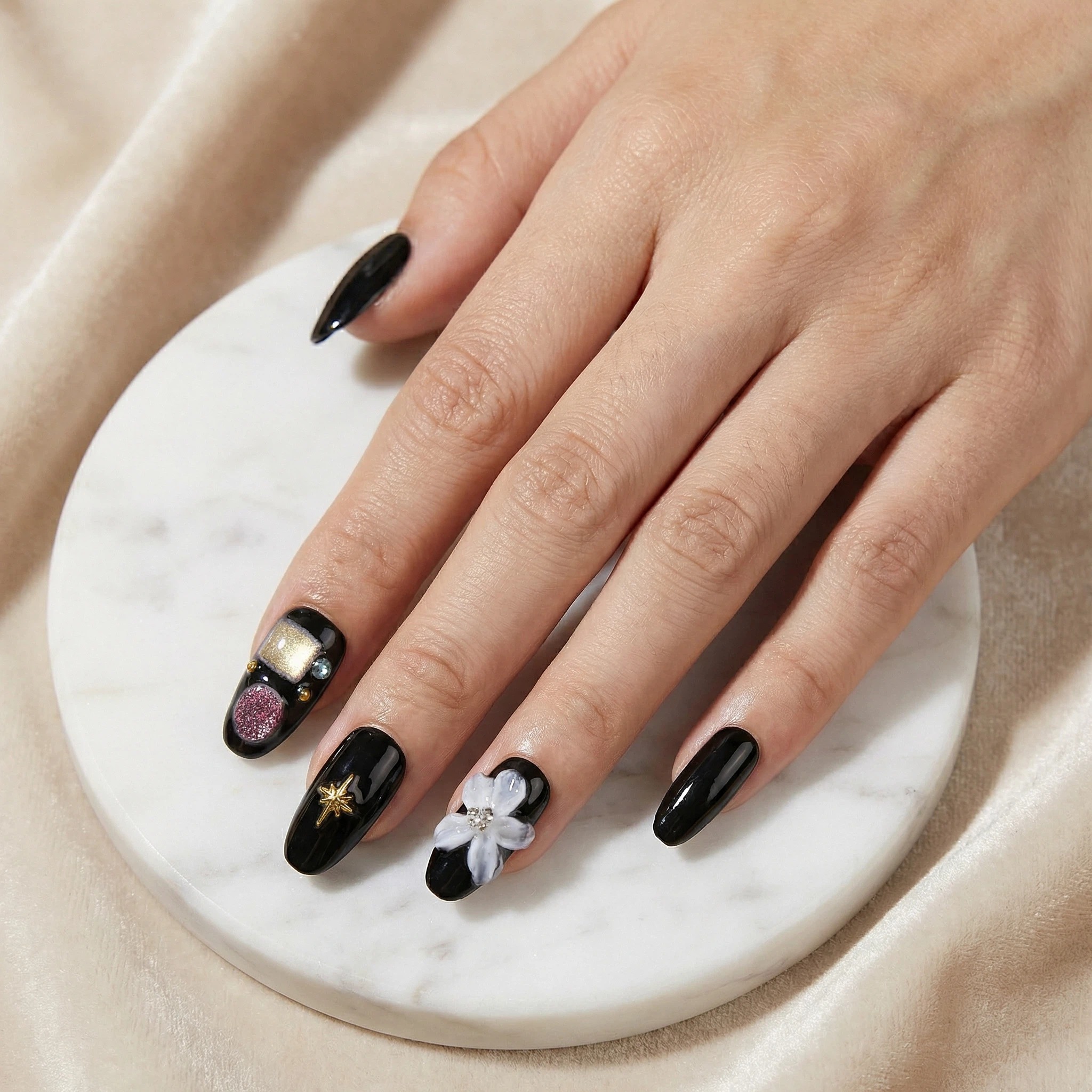 Glossy black handmade press-on nails on a hand with 3D white flower accent, gold star charm, and rhinestone details.