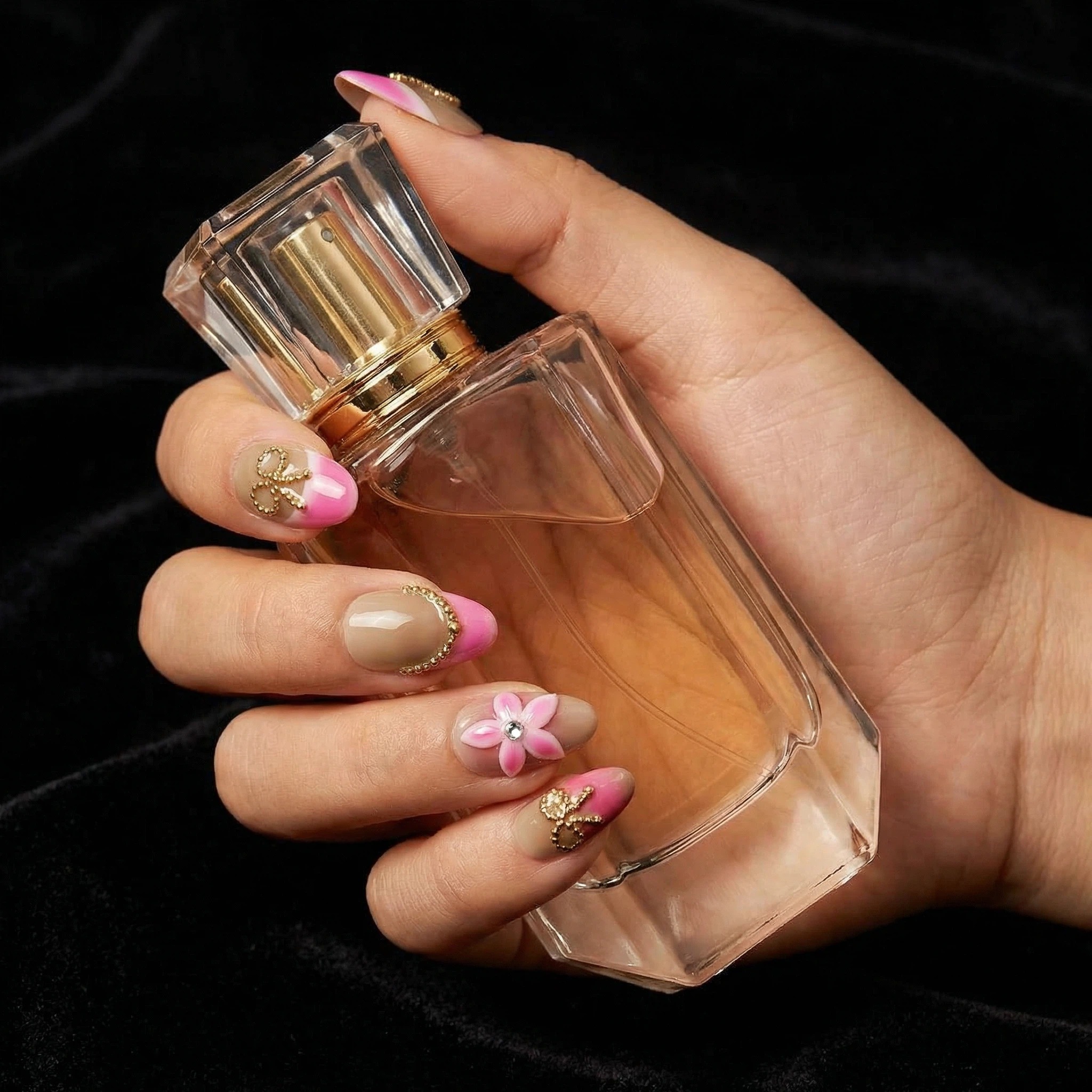 Close-up hand holding perfume bottle with pink French tip press-on nails and gold foil accents