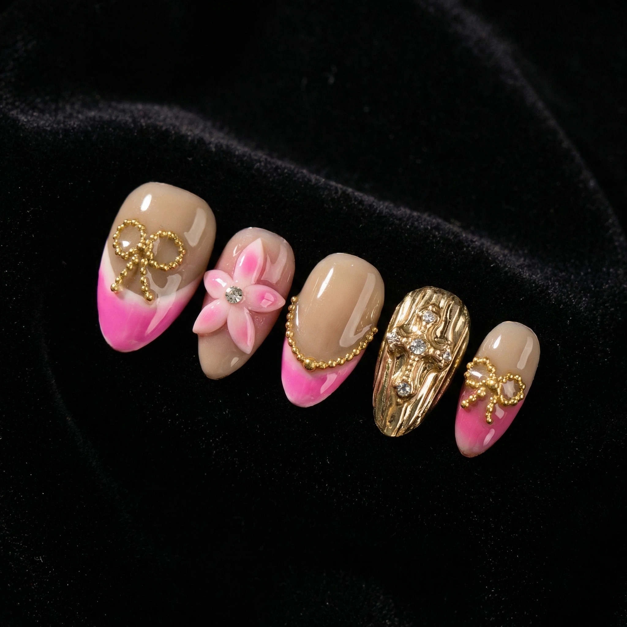 Close-up press-on nail set on black velvet featuring 3D pink flower and gold foil details