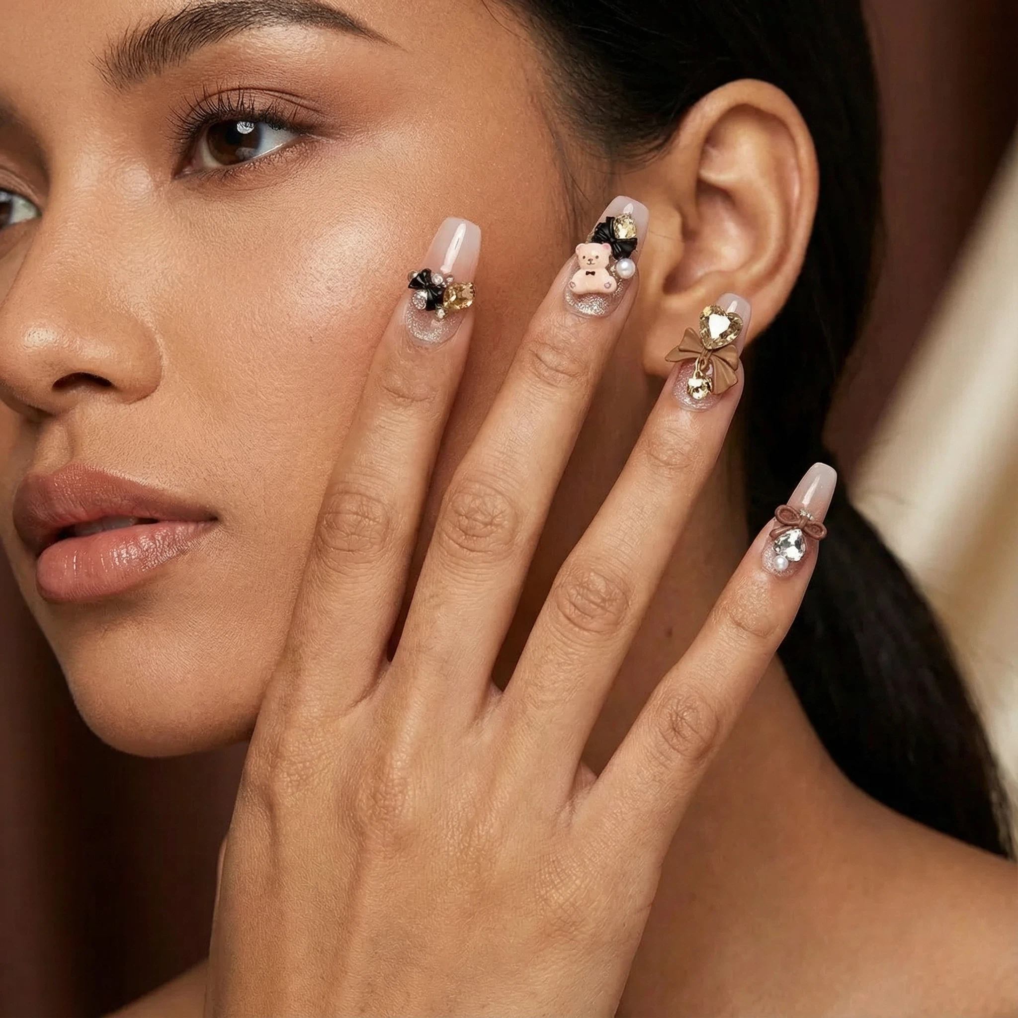 Model wearing glossy nude press-on nails with black details and 3D bow charm, salon-style finish