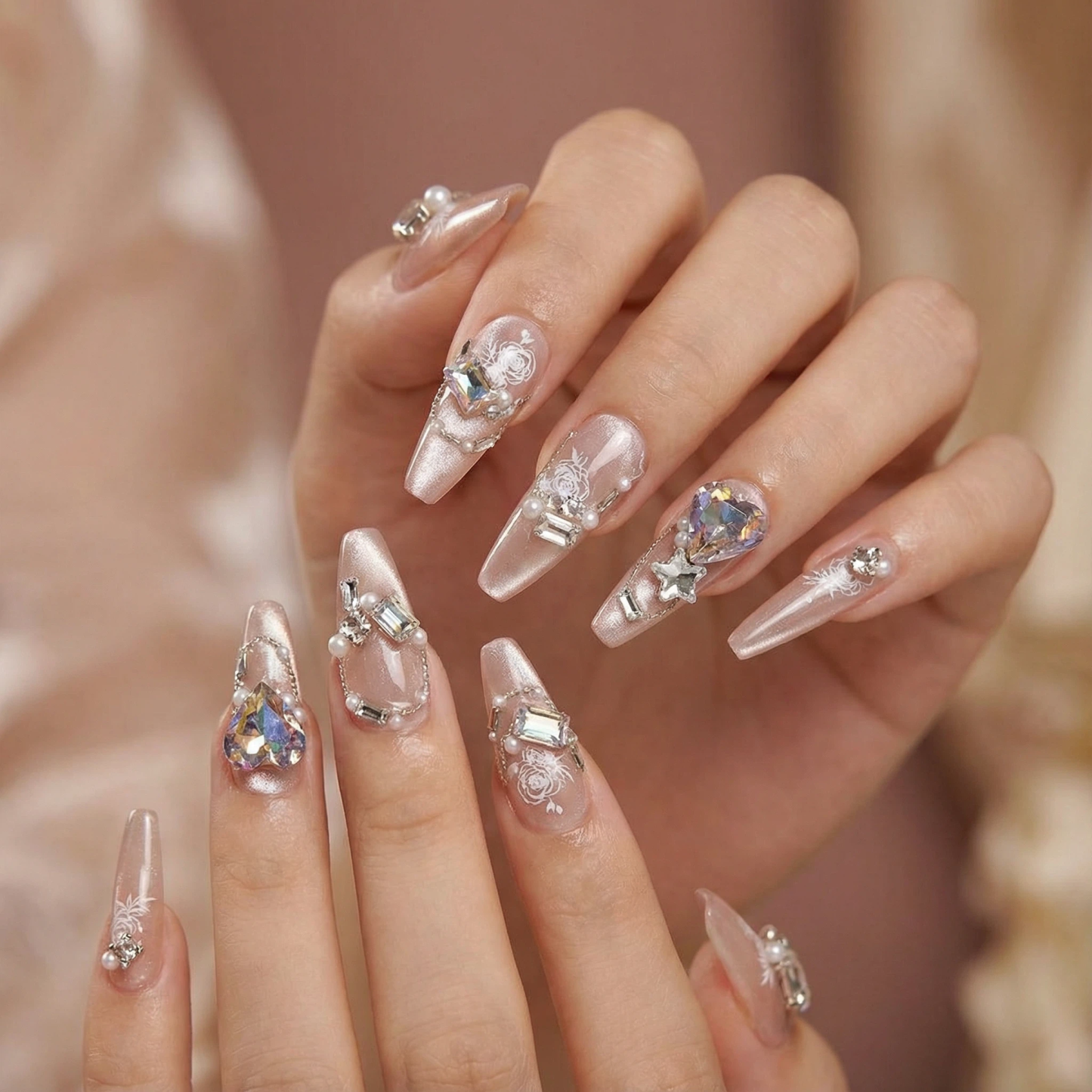 alt="Model wearing nude shimmer long press on nails with iridescent gems, pearls and white rose art"