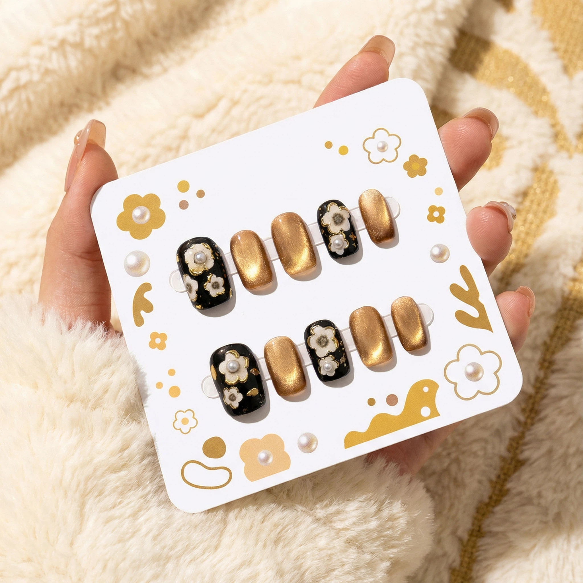 Black and metallic gold press-on nails with white daisy accents on a display card