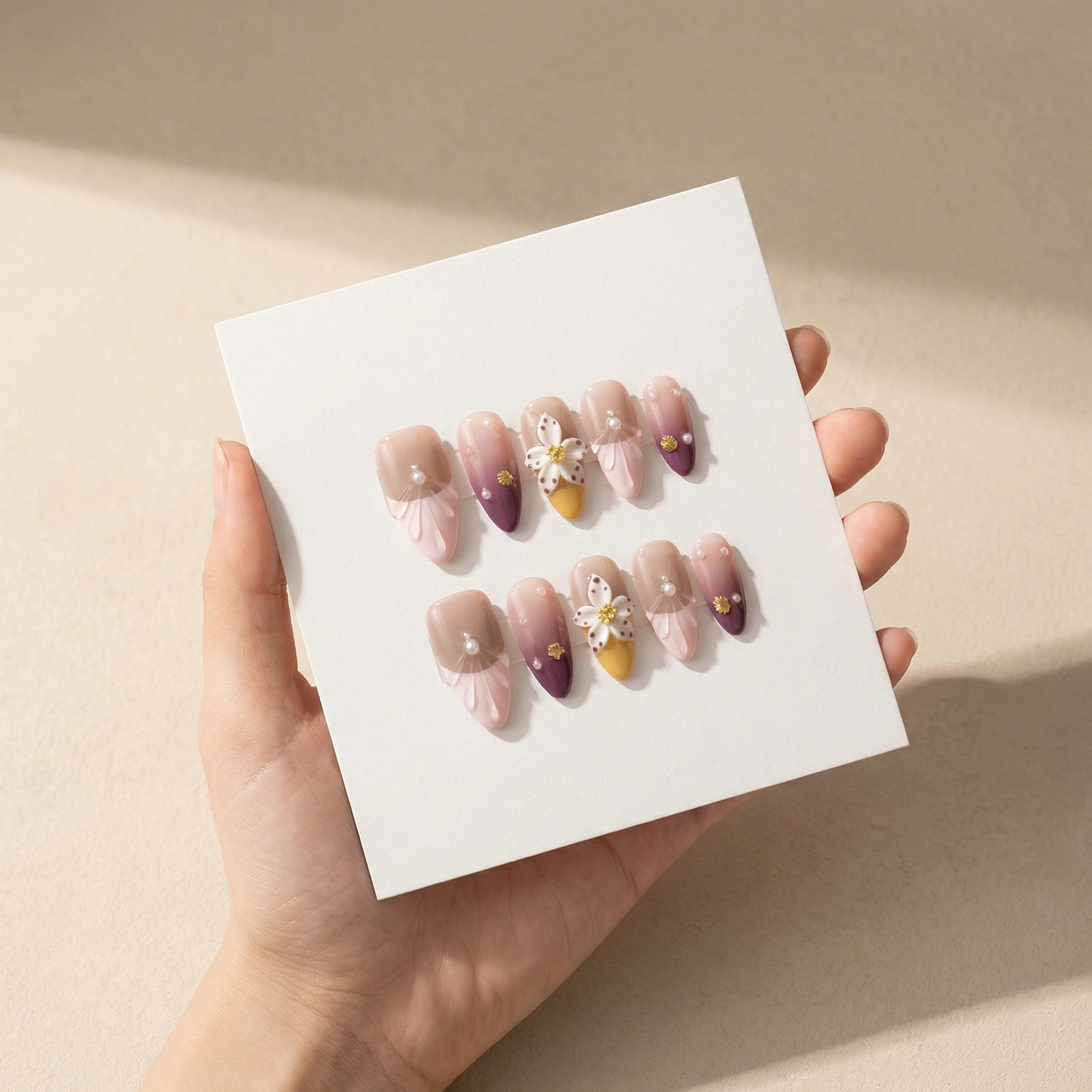 Cover: Hand holding mauve lilac ombré press-on nails set with floral and gold accents