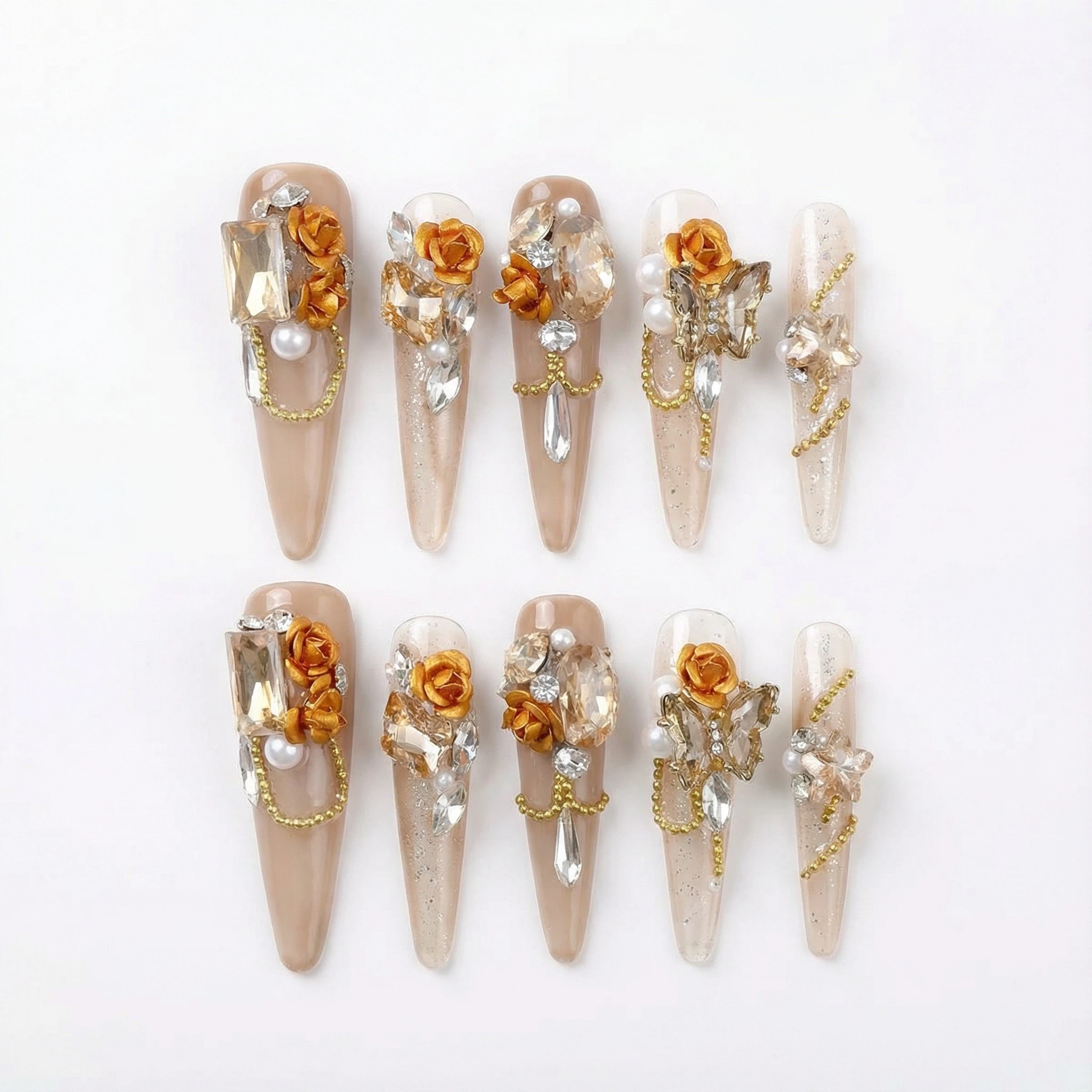 alt="Gold rose press on nails set with crystals, pearls and chain details on long nude stiletto tips"