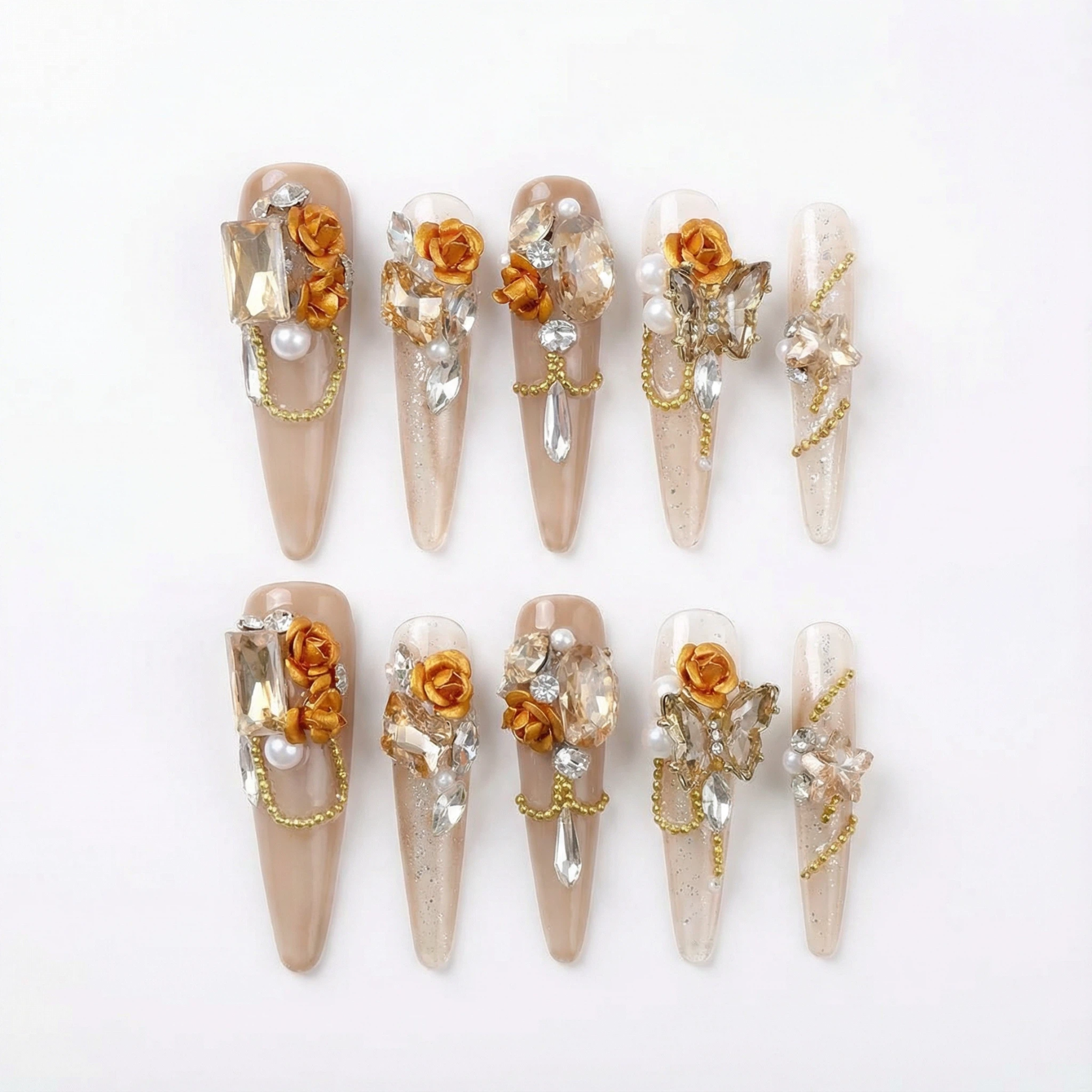 alt="Gold rose press on nails set with crystals, pearls and chain details on long nude stiletto tips"