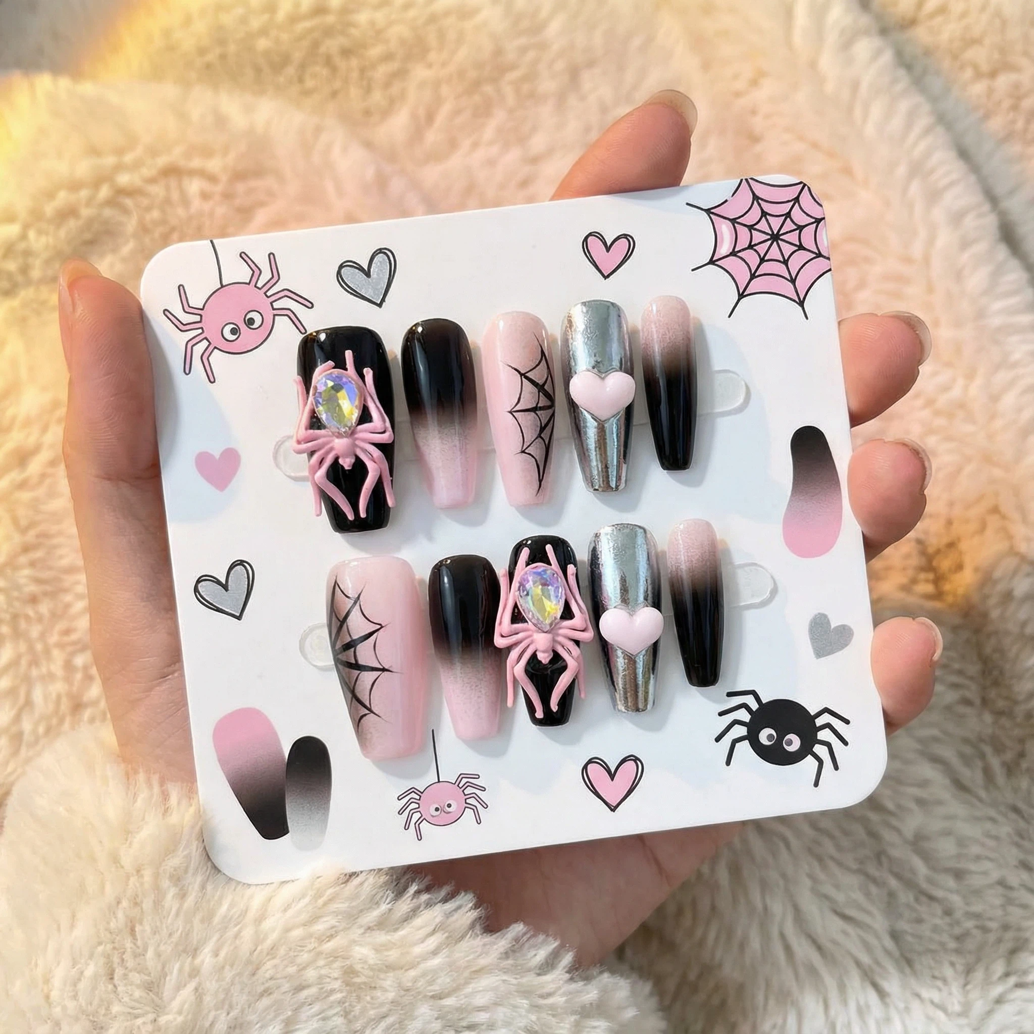 Hand holding display card with pink and black spider web press on nails set, glossy black ombré with 3D spider accents