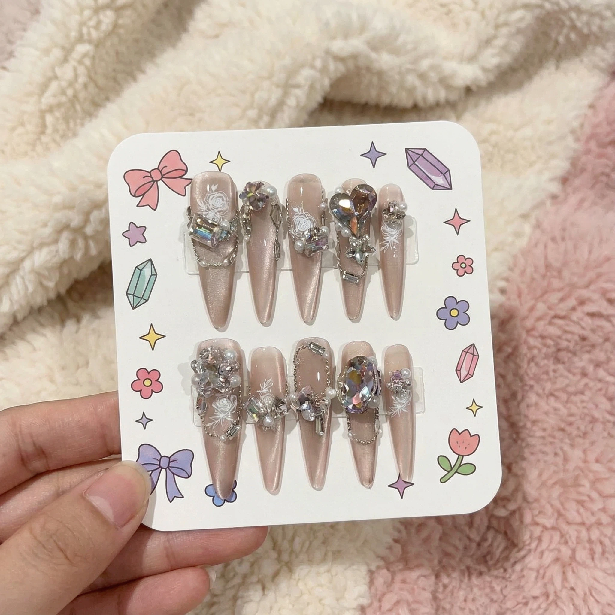 alt="Packaging card with nude shimmer long almond press on nails set decorated with iridescent gems and pearls"
