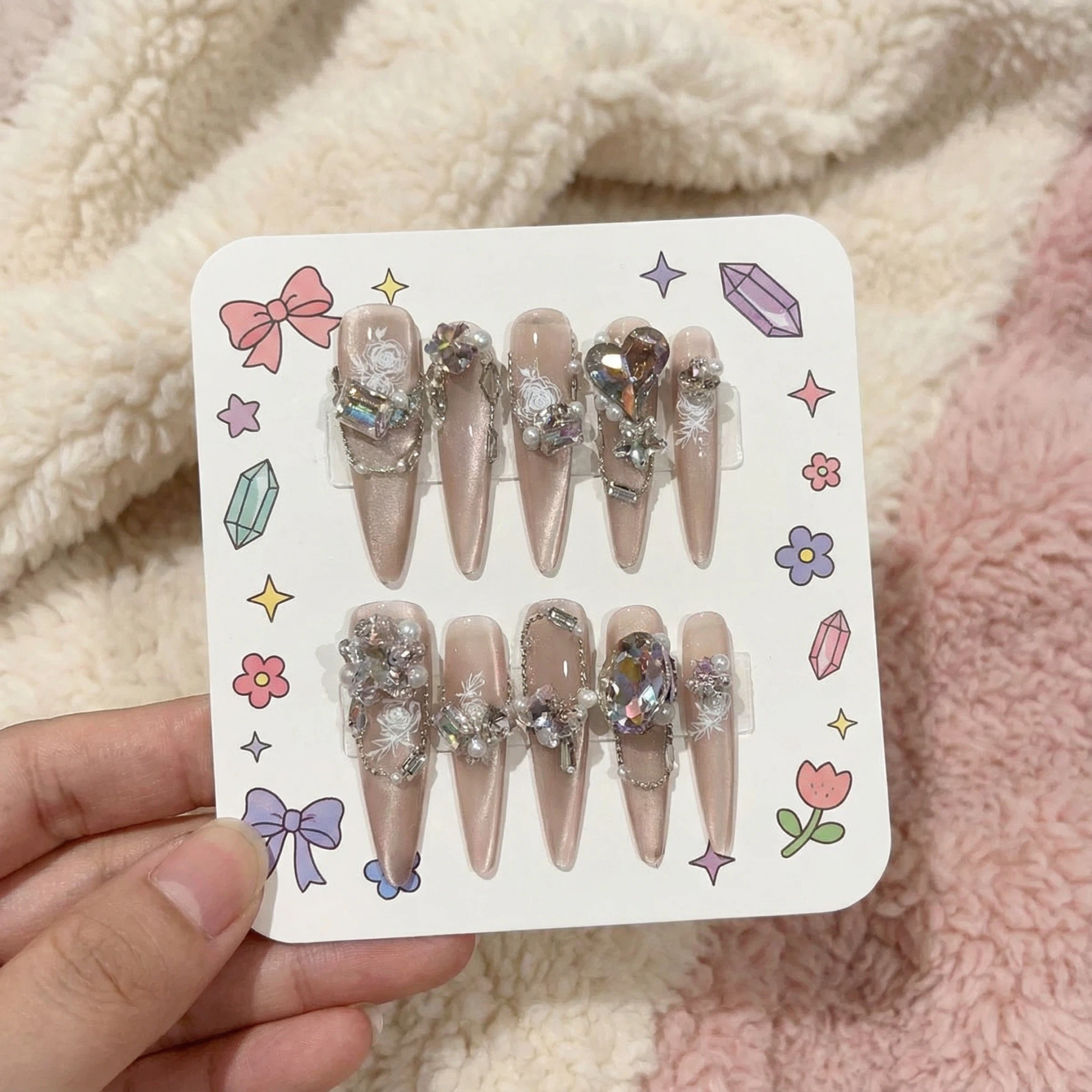 alt="Packaging card with nude shimmer long almond press on nails set decorated with iridescent gems and pearls"