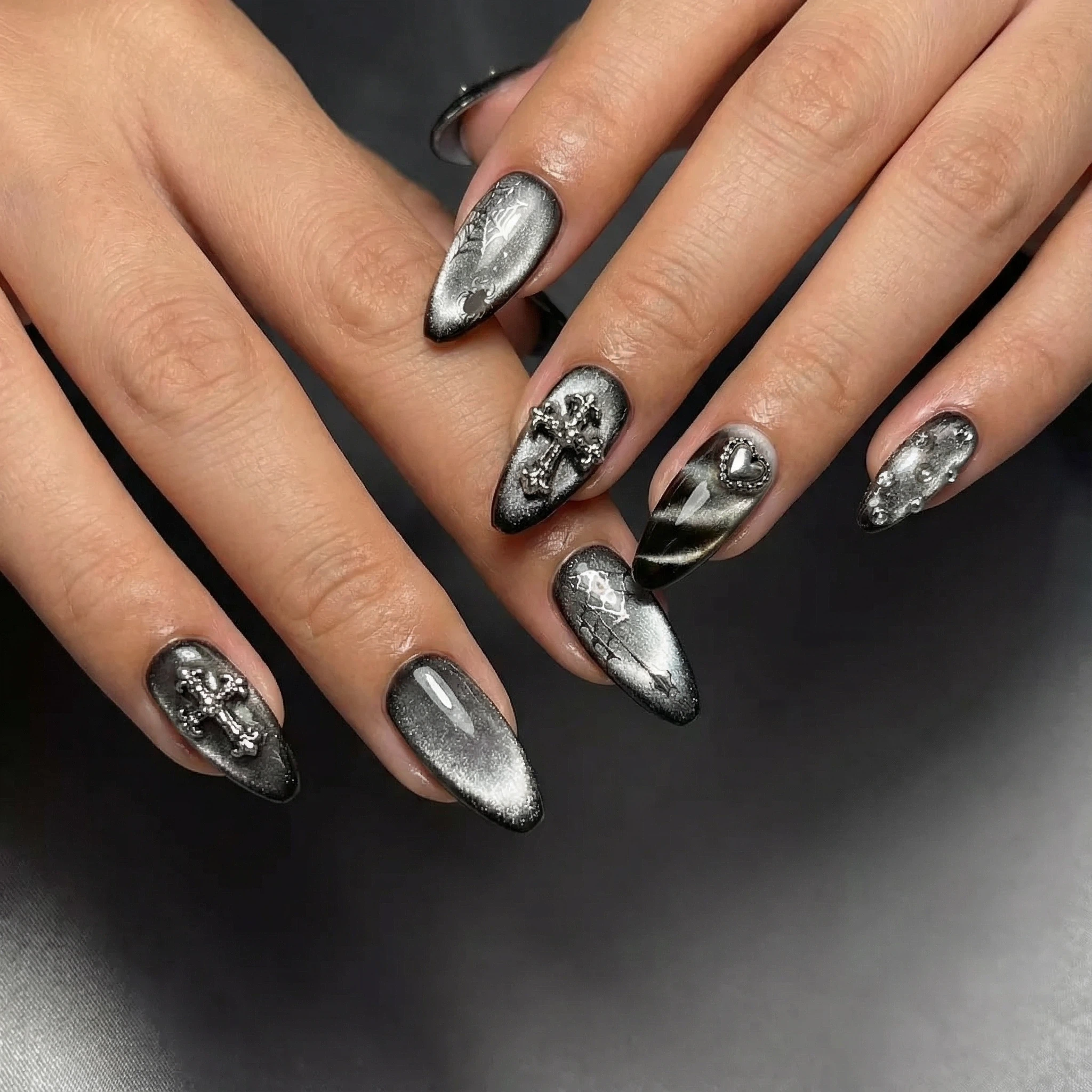 Close-up of hands showing gunmetal press-on nails with cross, heart, and textured metallic designs