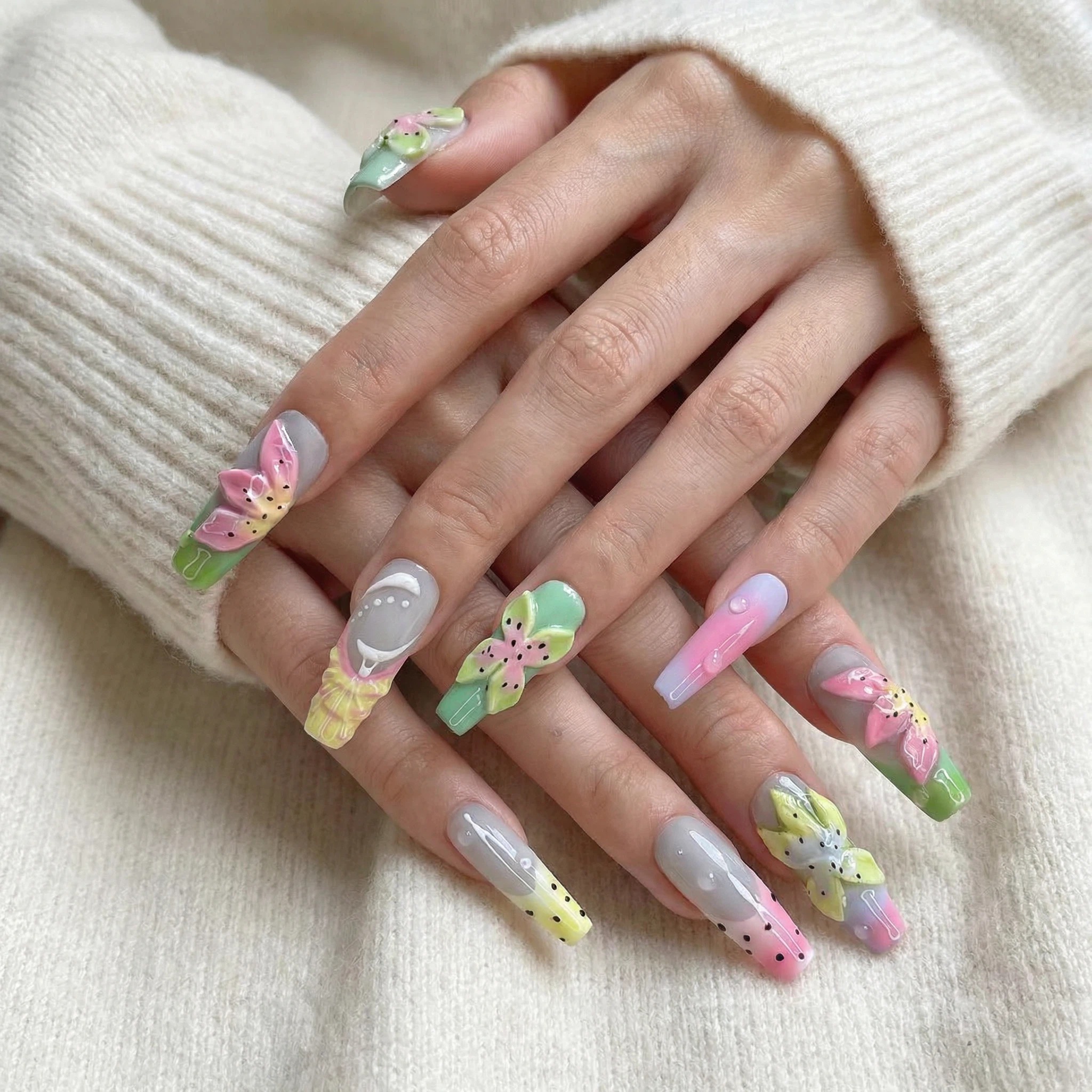 Hands wearing pastel ombré press-on nails with colorful flower details, long coffin shape