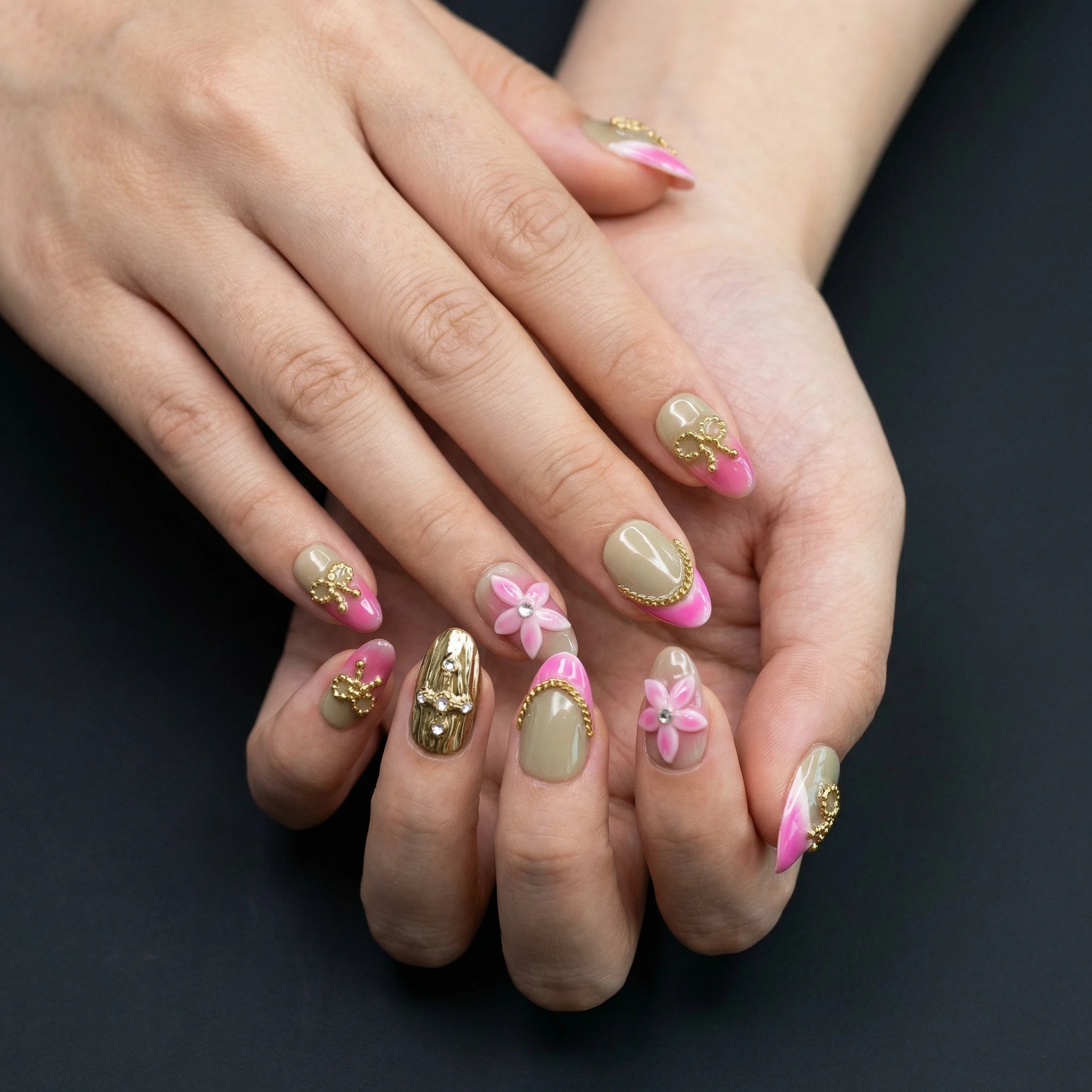 Hands clasped showing pink French tip press-on nails with 3D flower charm and gold shimmer