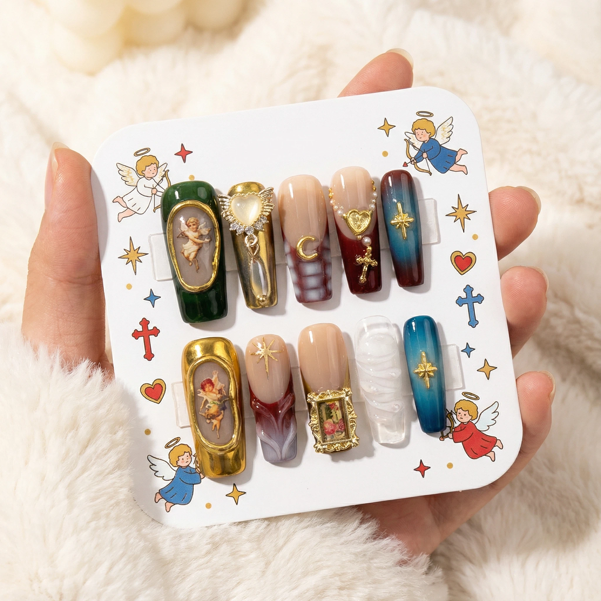 Press-on nails set on a display card — emerald green, burgundy and blue nails with gold cross and baroque frame accents.