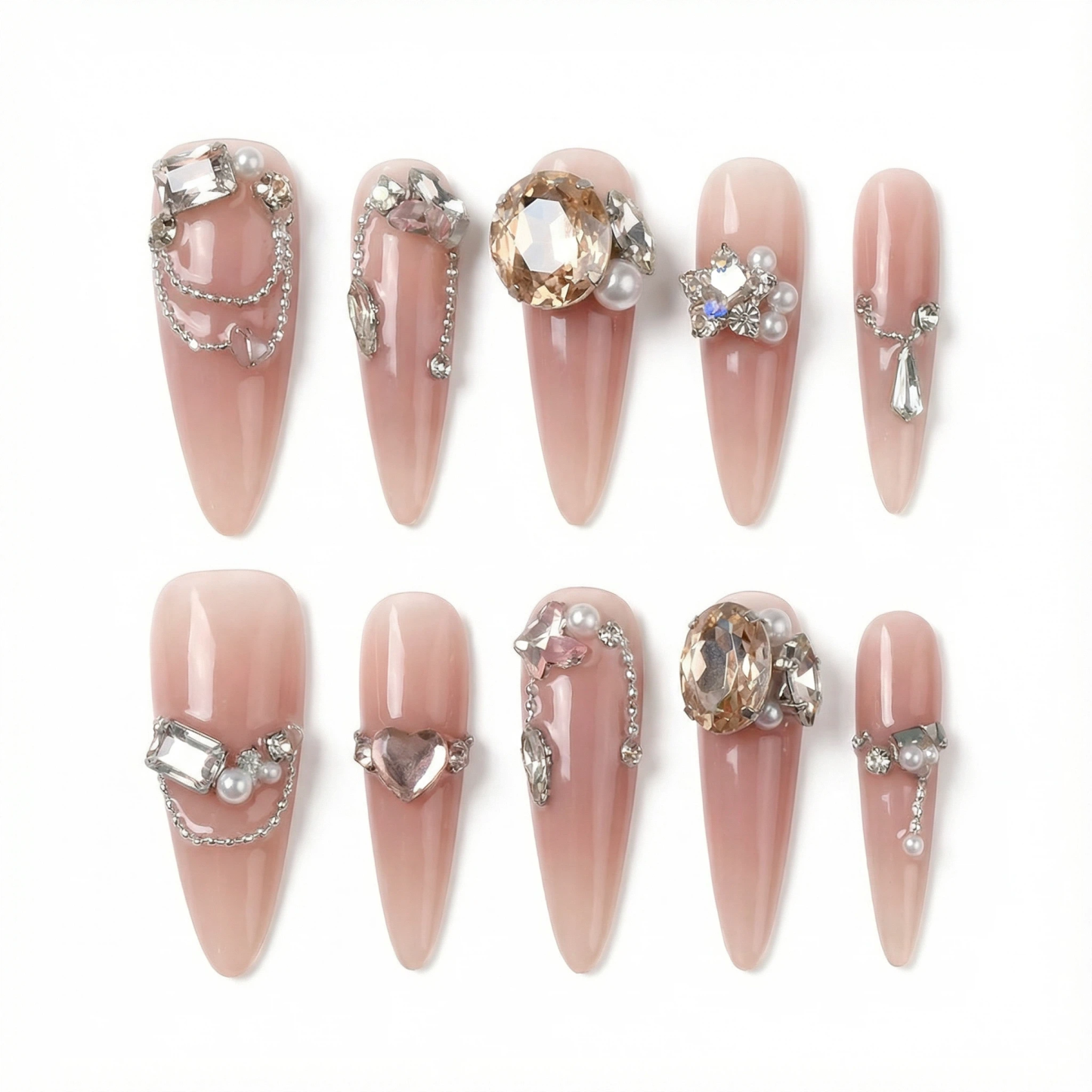 Flat lay of nude pink long stiletto fake nails featuring 3D rhinestones, pearls and chain accents on a white background.