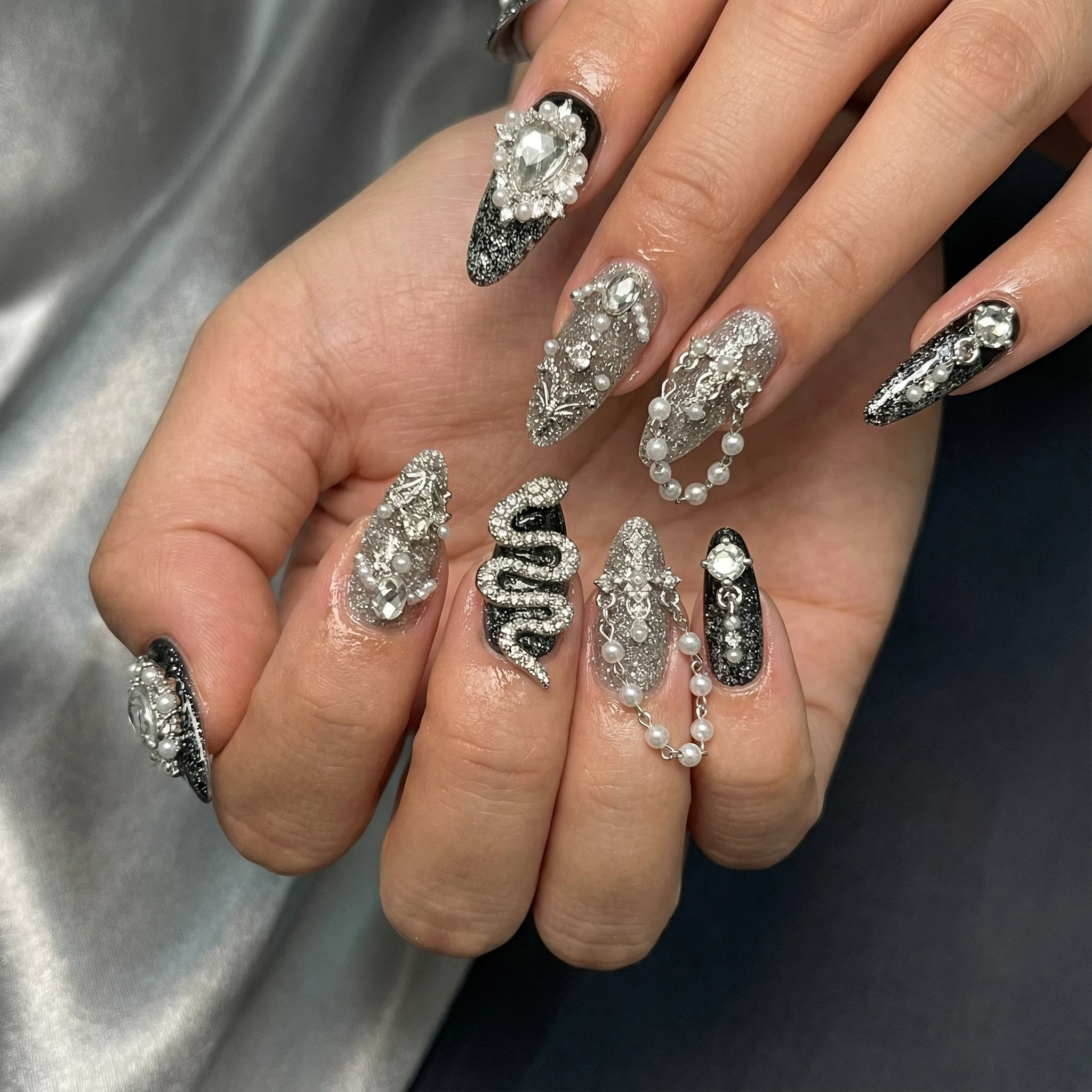 Hand wearing black-silver rhinestone press-on nails featuring a statement snake and crystal accents