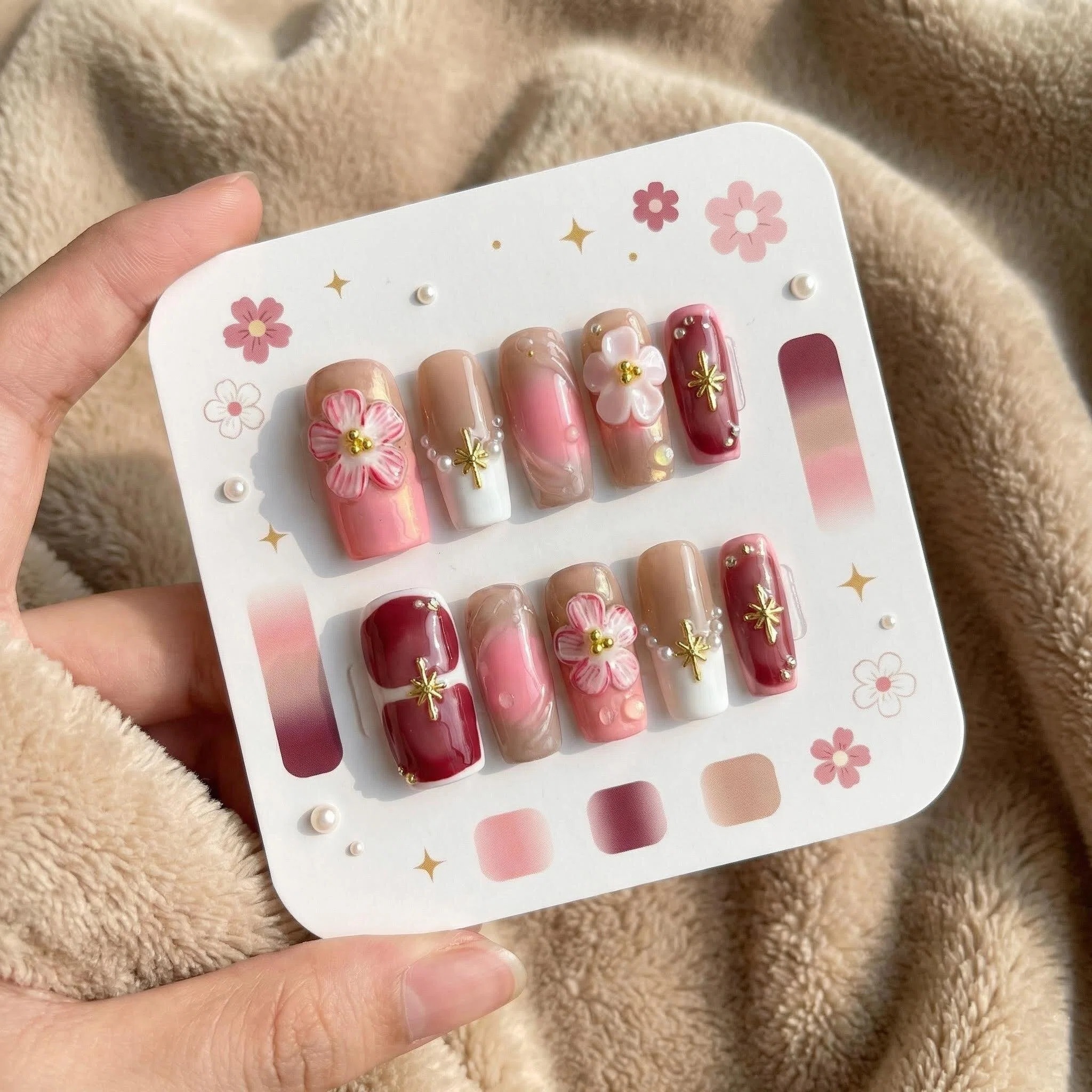 Blush pink and burgundy floral press-on nails set with 3D flowers, pearls, and gold charm accents on display card