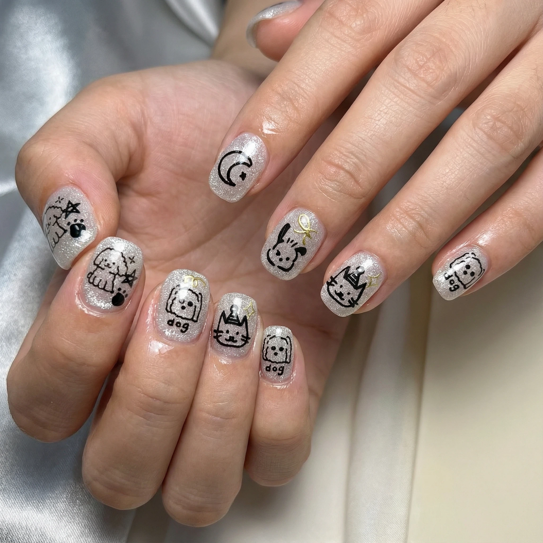 hands wearing silver glitter short press on nails with black pet doodle designs