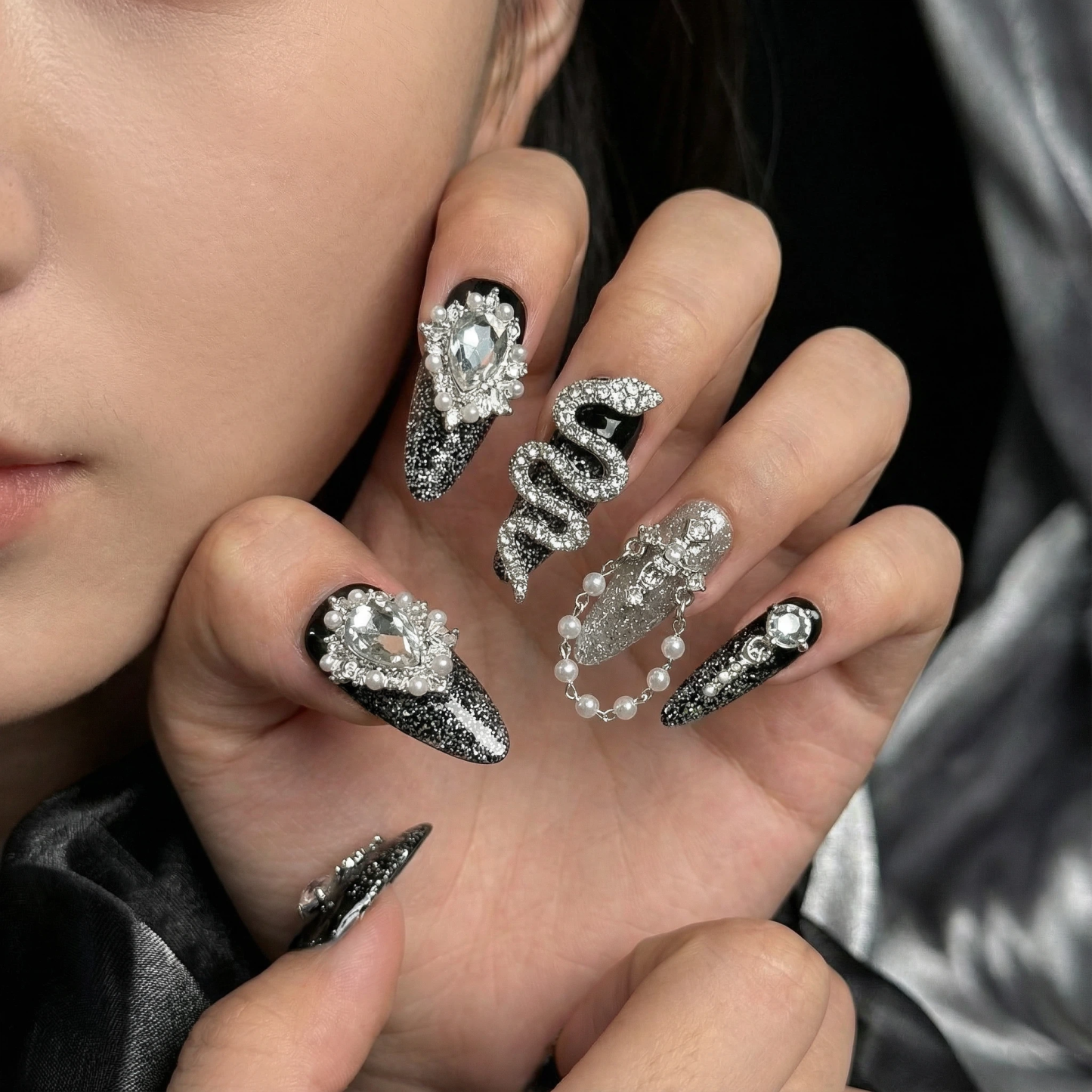 Close-up glam look of black and silver stiletto press-on nails with crystal and pearl details